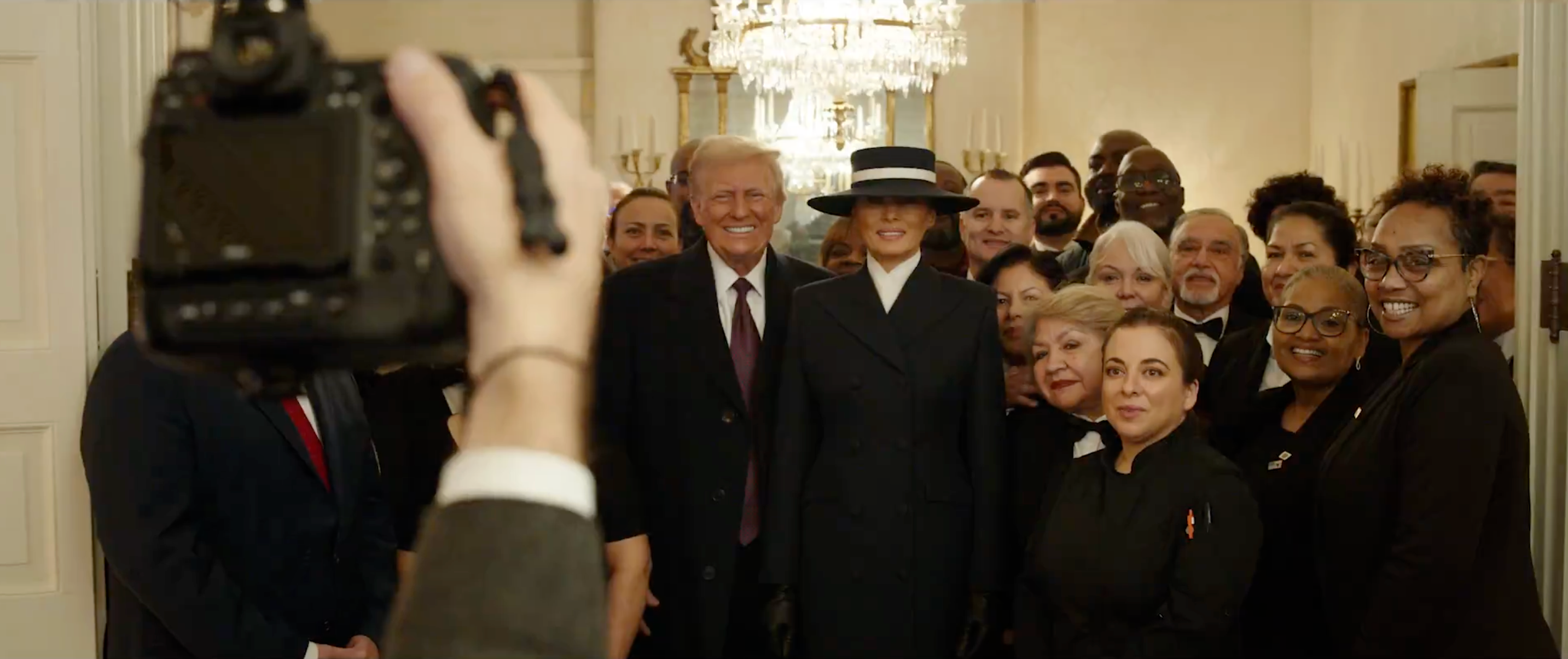 Gruppebilde av formelt kledde personer som poserer innendørs med smilende uttrykk. Et kamera er synlig i forgrunnen