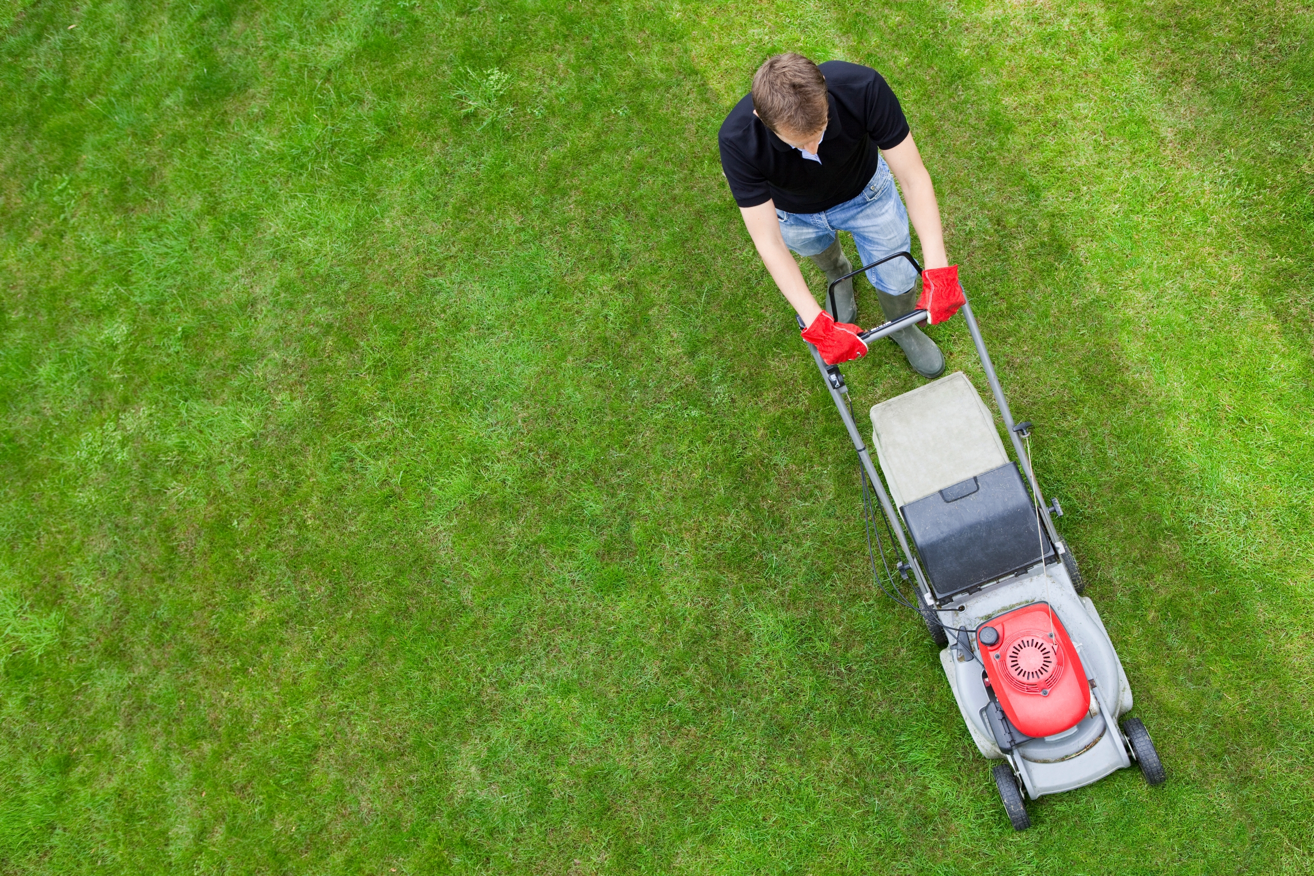 Person mowing tract with a propulsion mower, seen from above. They're wearing a achromatic garment and jeans, focusing connected the task astatine hand