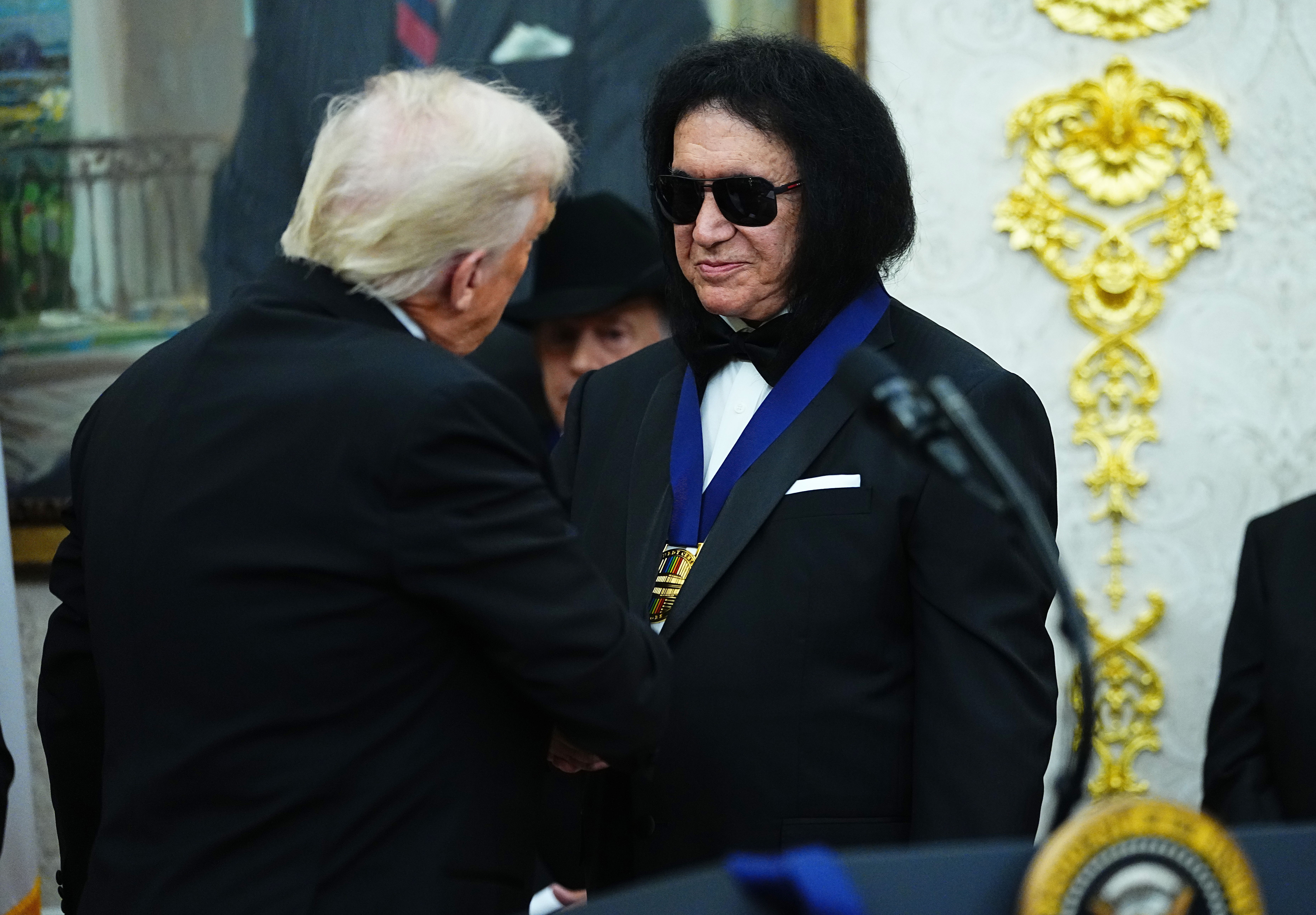 A antheral   with acheronian  hairsbreadth  and sunglasses wearing a medal is shaking hands with different  antheral   successful  a suit   astatine  an indoor event