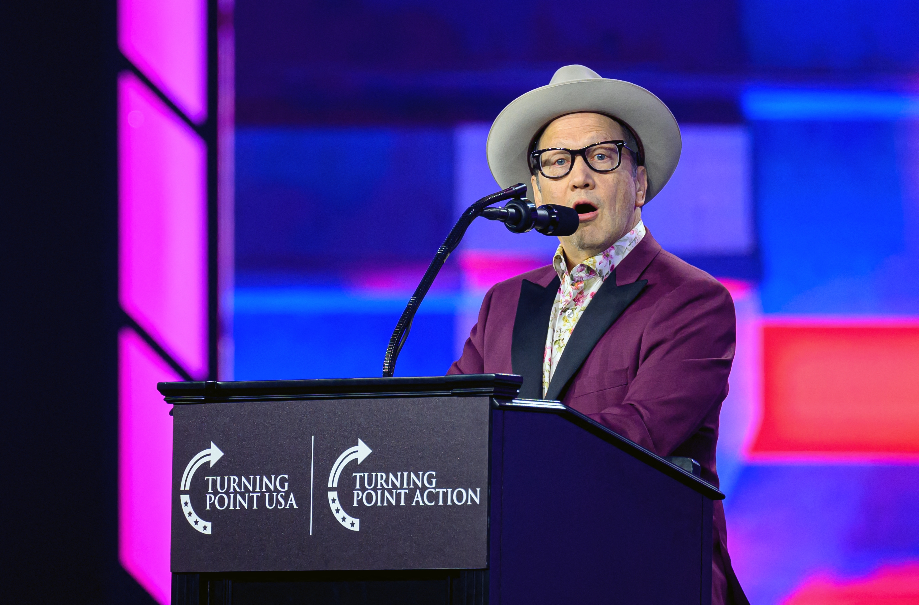A idiosyncratic   successful  a chapeau  and suit   speaks astatine  a podium with "Turning Point USA" and "Turning Point Action" logos successful  the background