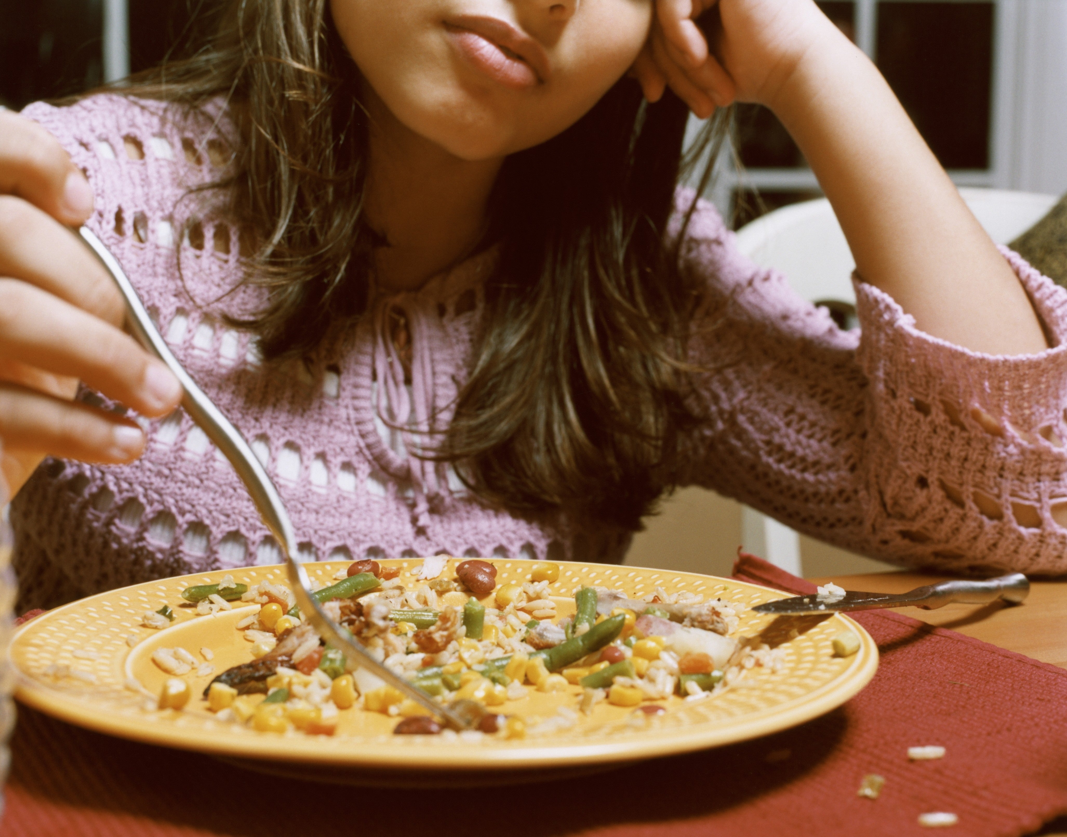 Person successful a knitted sweater looking astatine a sheet of mixed crockery with a fork, appearing contemplative