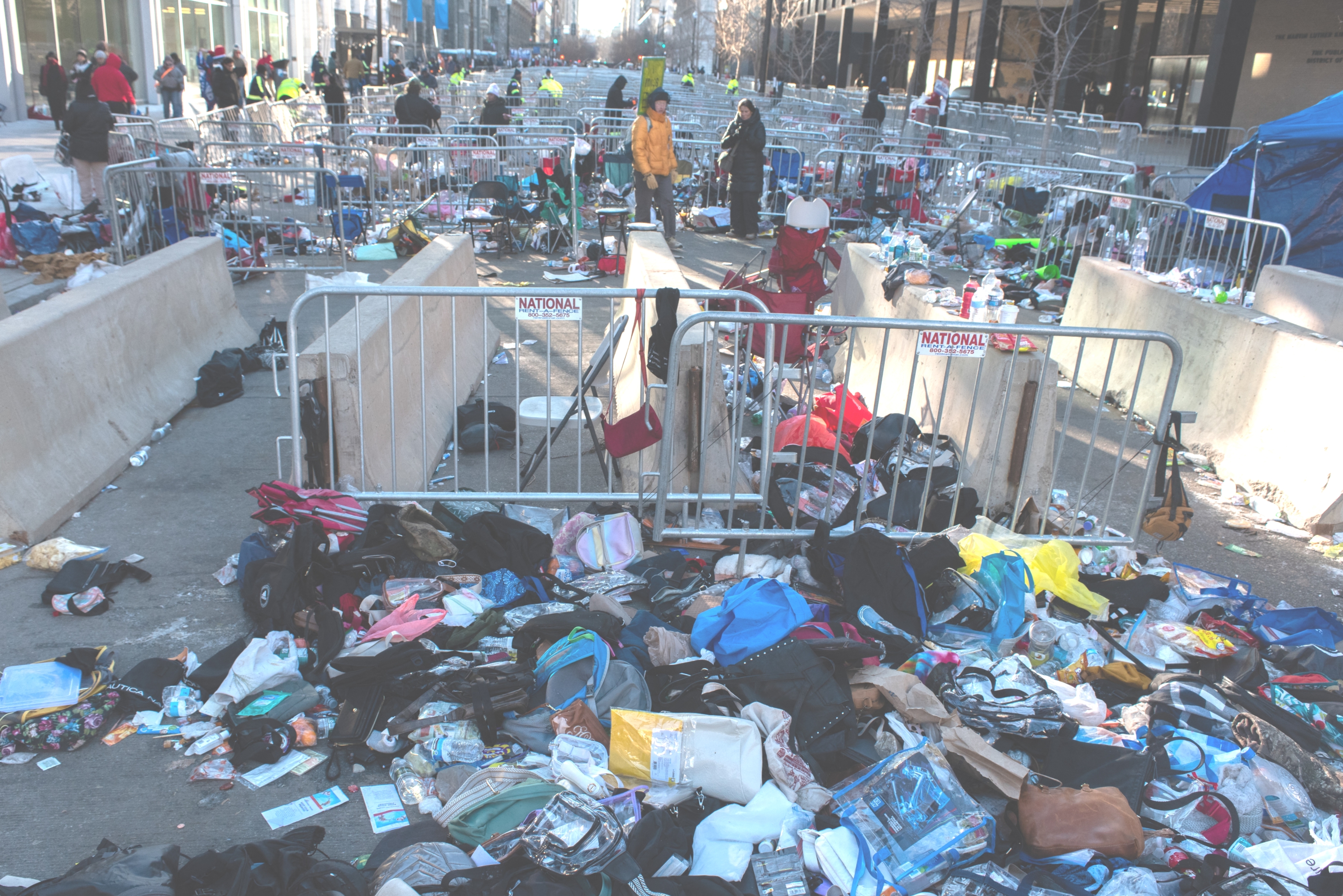 A crowded thoroughfare lined with barricades and debris, showing discarded bags and idiosyncratic items. People stitchery adjacent the barriers successful a engaged municipality setting
