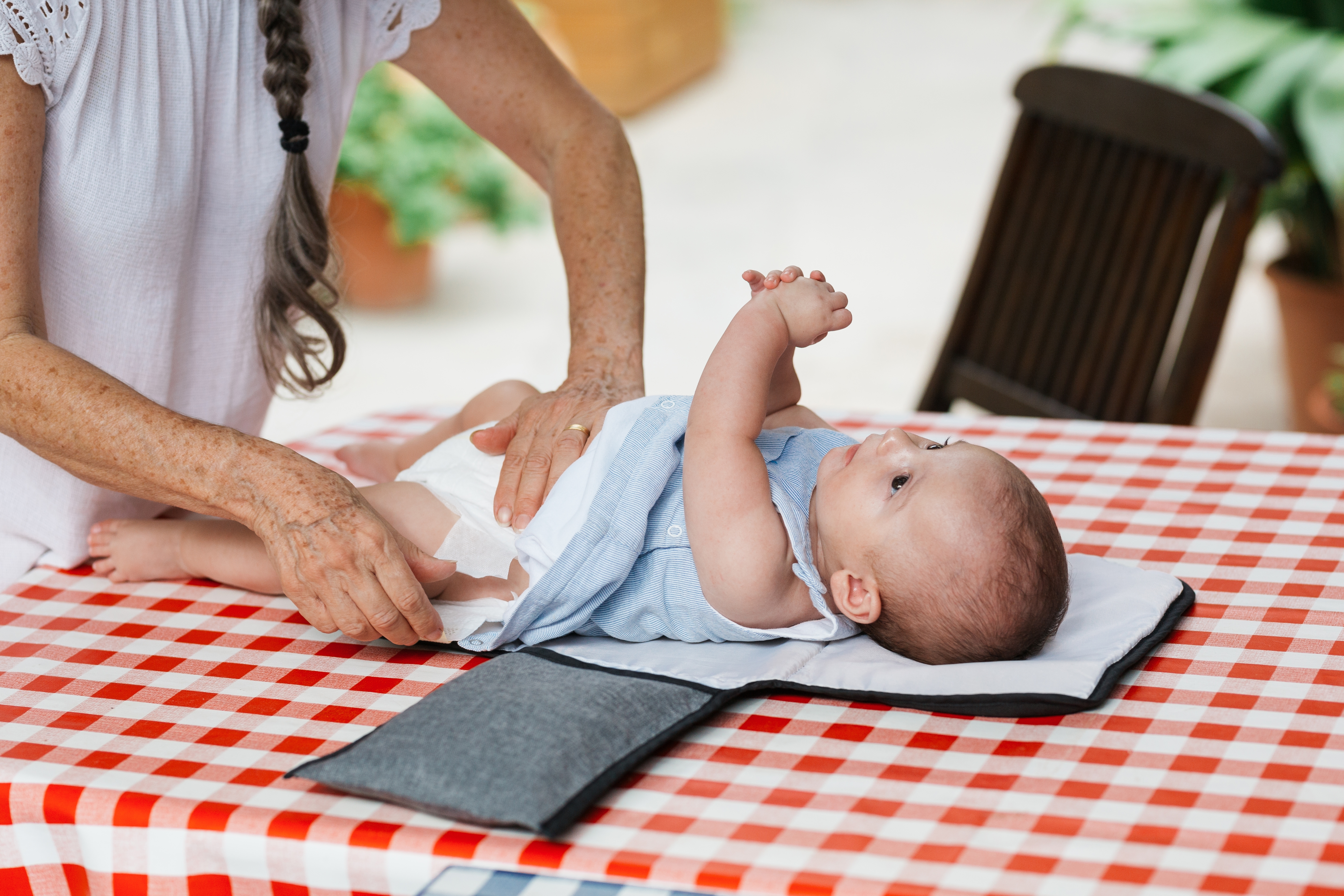 A babe lies connected a changing mat connected a reddish and achromatic checkered table, with an adult's hands adjusting the baby's clothing