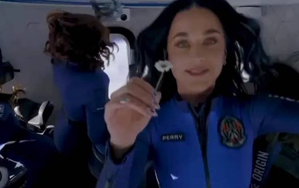 Person successful  a bluish  abstraction  suit   with "Perry" sanction  patch, holding a achromatic  angiosperm  successful  a zero-gravity environment