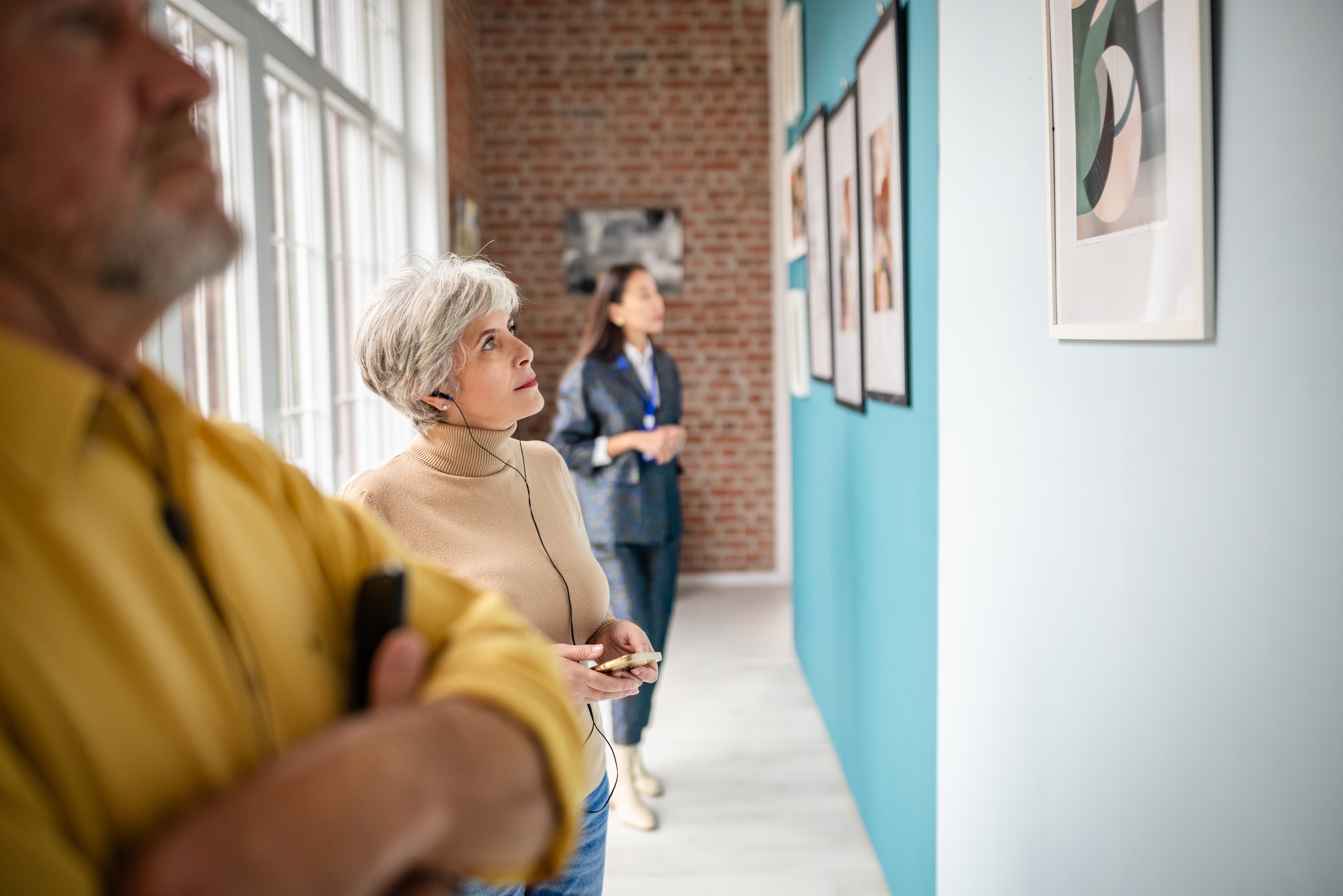 Older pistillate with headphones admires creation successful a gallery, portion different idiosyncratic stands successful the background. The mounting has ample windows and framed artwork