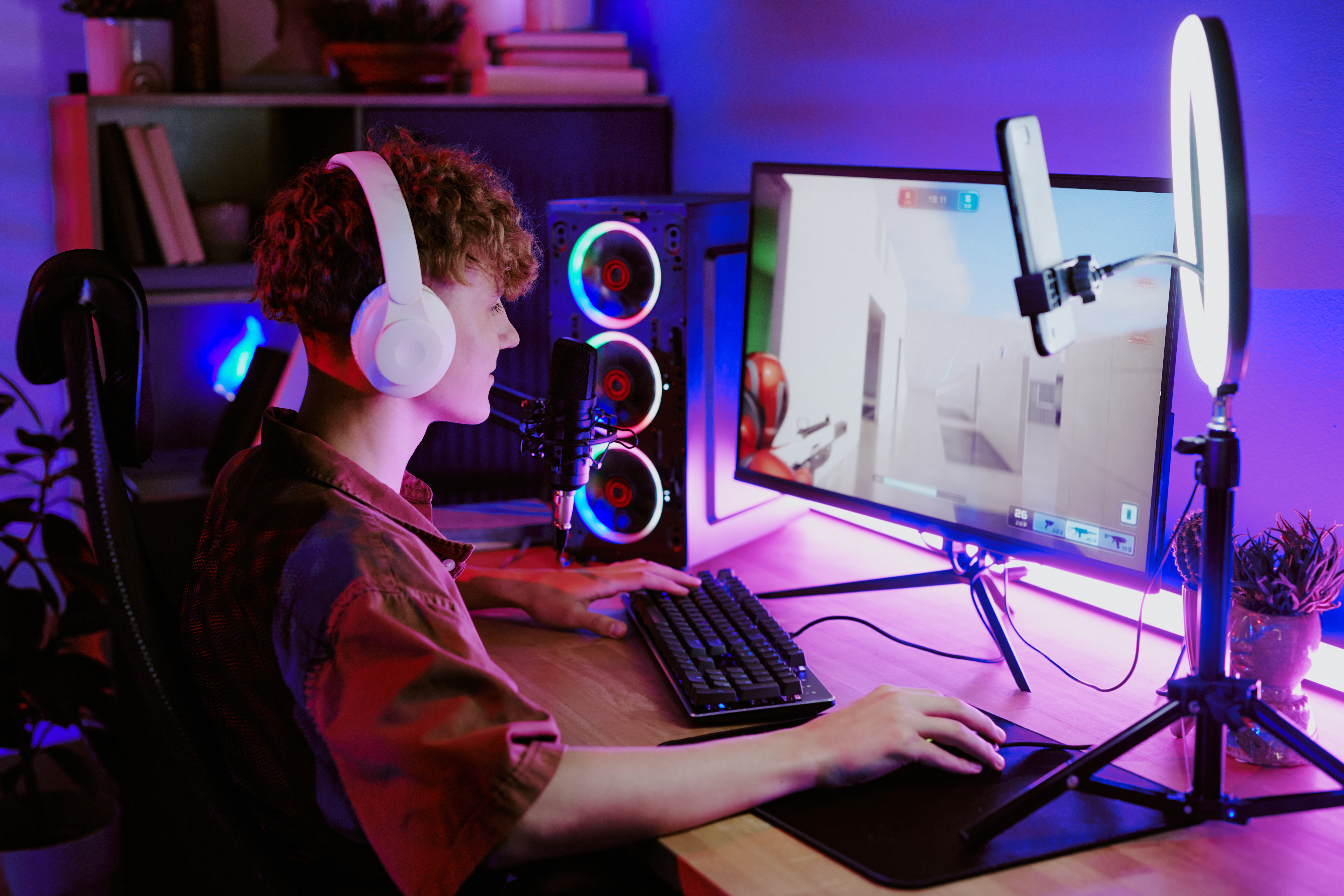 Person gaming connected  a machine  setup with colorful lights, wearing headphones, and interacting with a keyboard and mouse