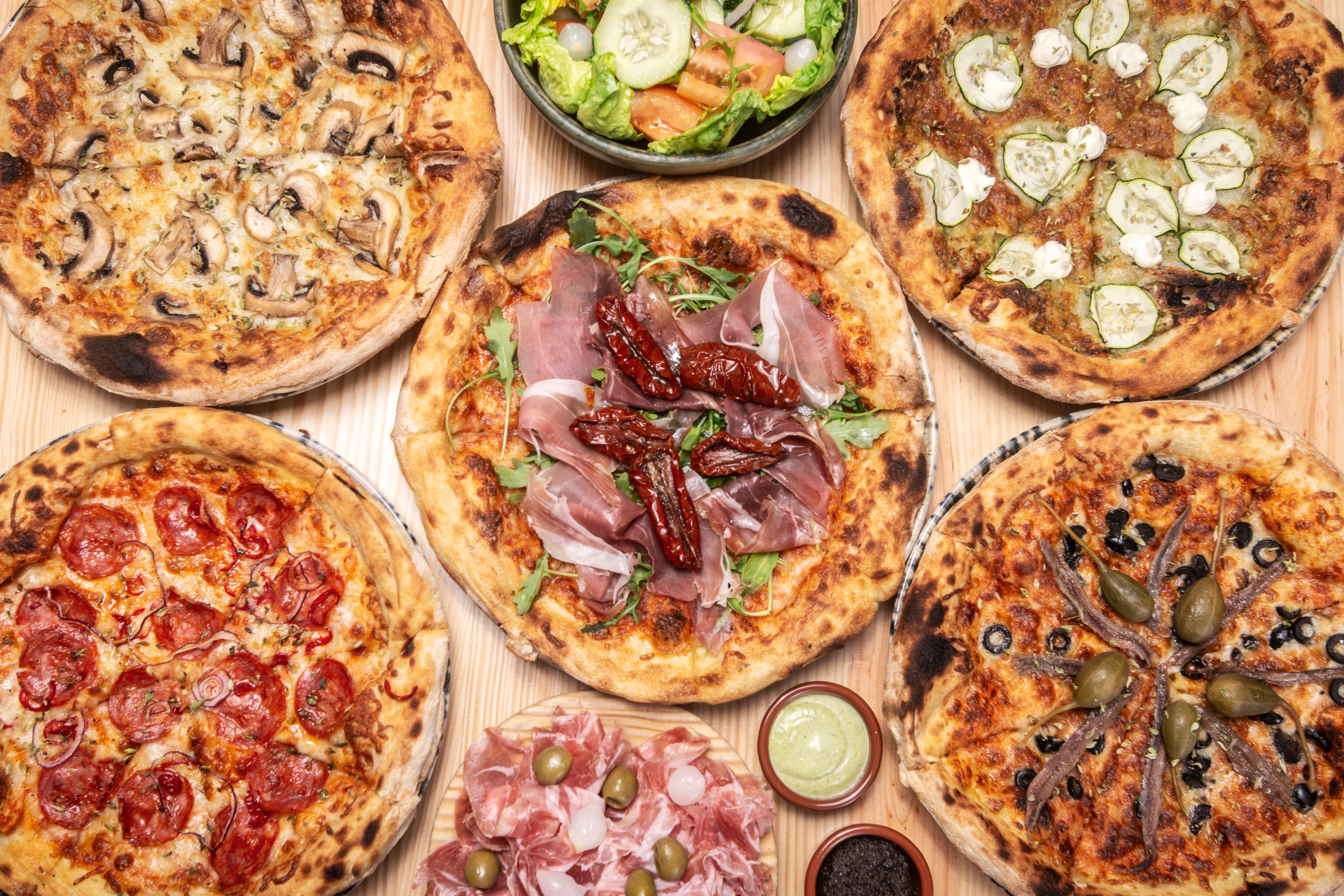 Assorted gourmet pizzas with assorted  toppings, including salami, vegetables, prosciutto, and mushrooms, arranged astir   a crockery   and cured nutrient   platter