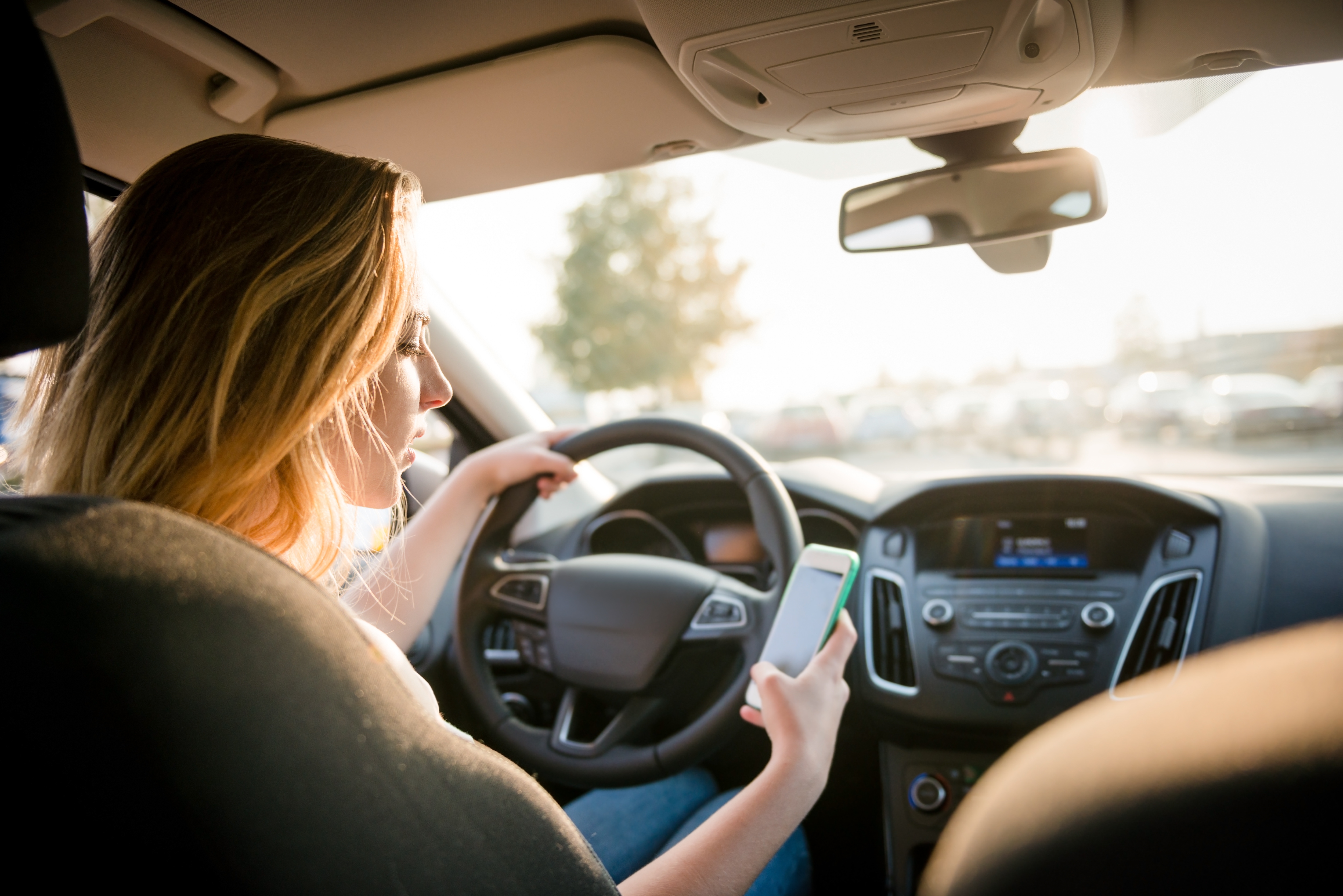 Person successful  a car   holding a smartphone portion    driving, looking towards the road. The country   suggests utilizing a telephone  portion    driving
