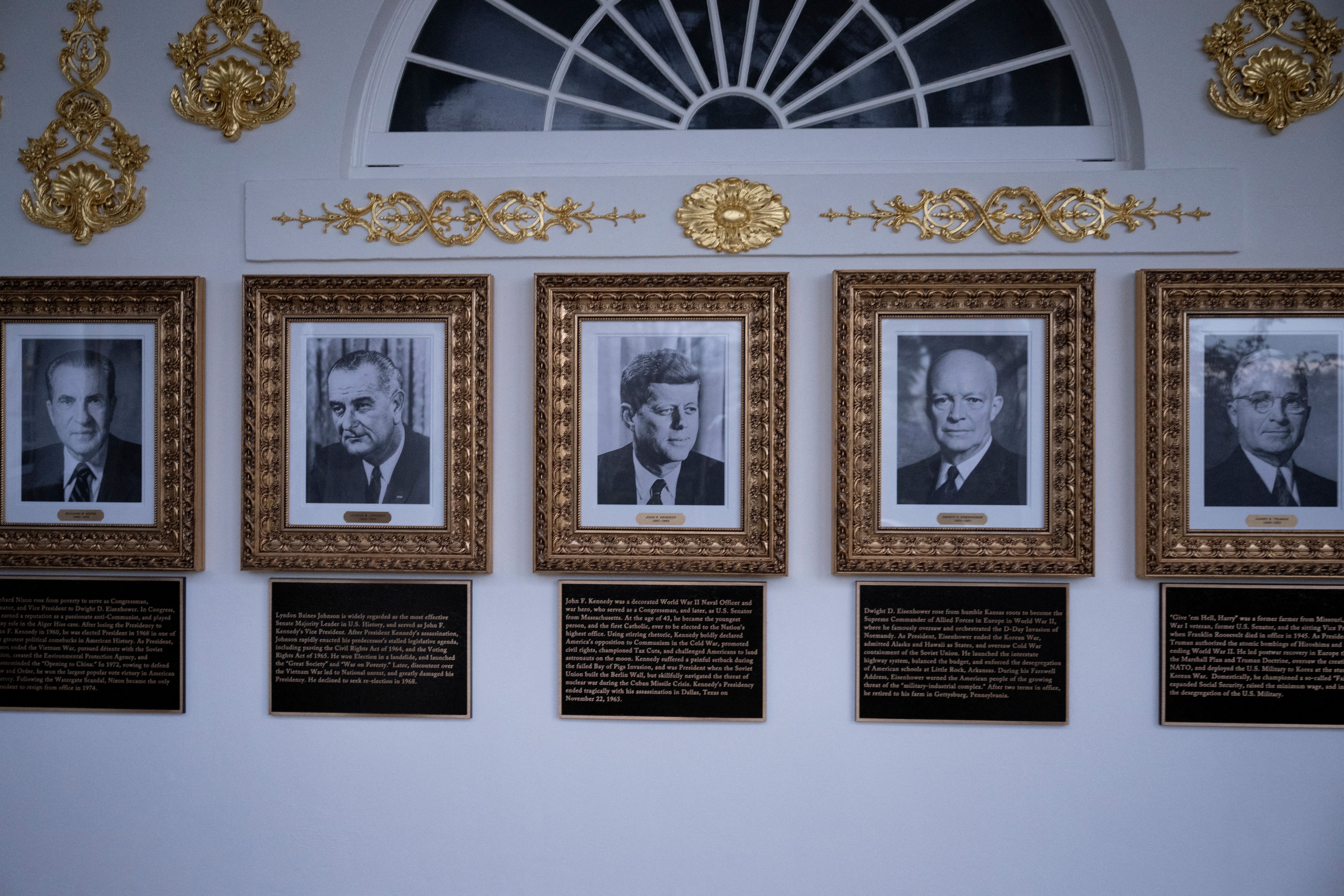 Fem innrammede portretter av amerikanske presidenter med gyldne dekorative detaljer på veggen; plaketter oppsummerer deres prestasjoner under hvert portrett