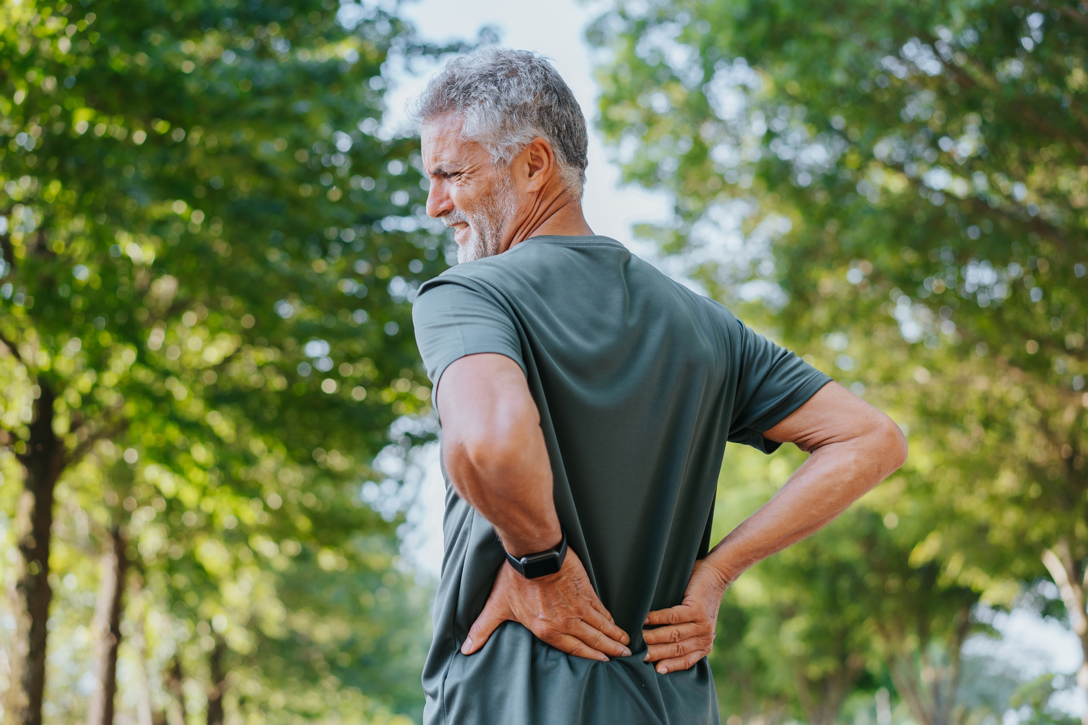 Man outdoors holding his little   back, appearing successful  discomfort. Trees and a agleam  entity  are successful  the background, suggesting a quality  setting