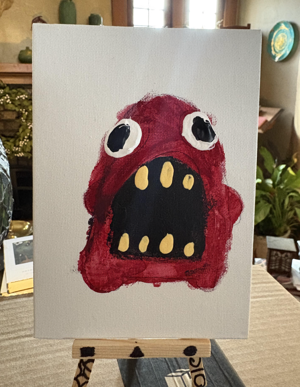 Child's coating  of a reddish  monster with ample  eyes and a wide   mouth, displayed connected  an easel successful  a cozy country   setting