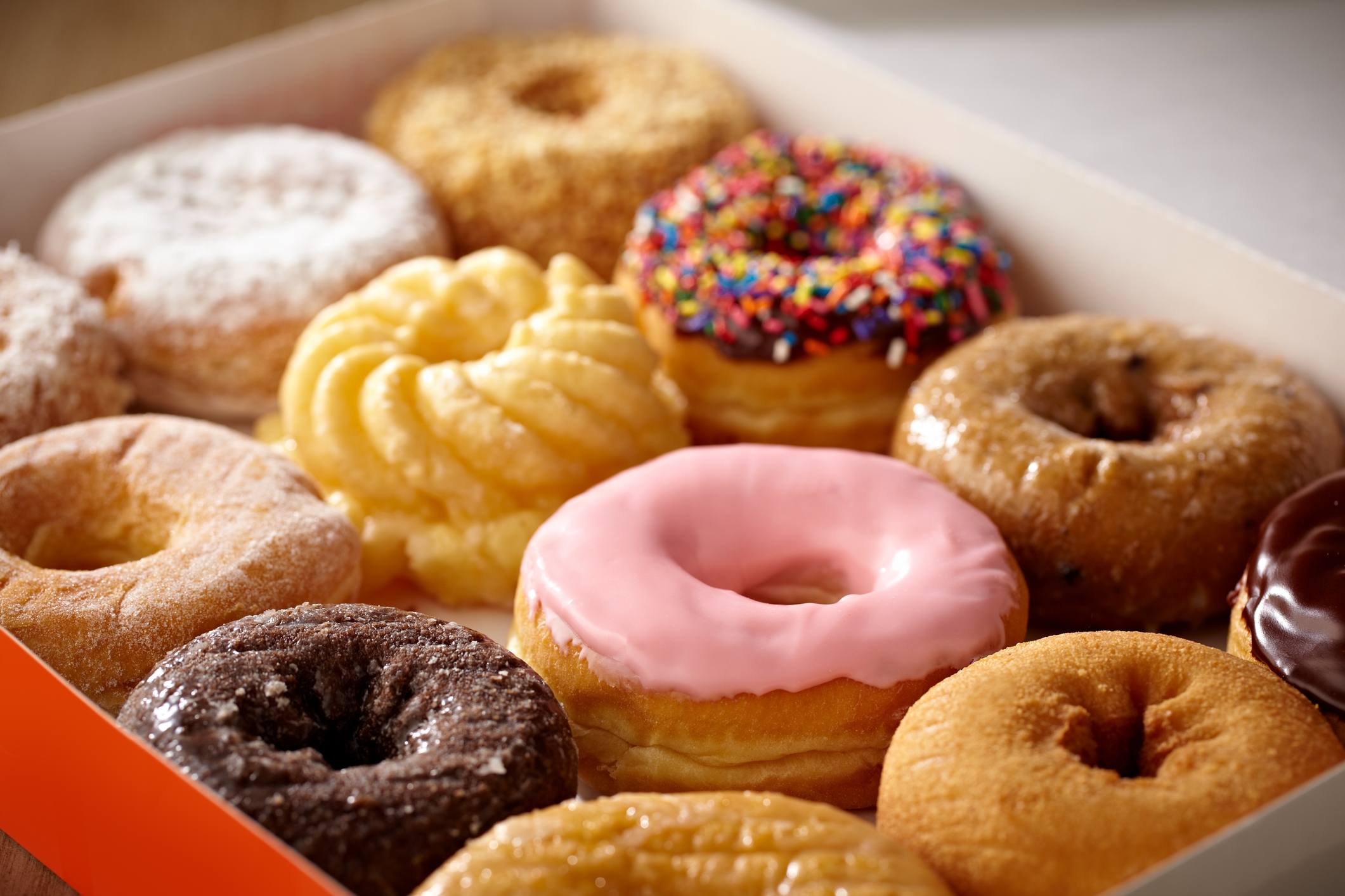 A container  of assorted donuts, including a pinkish  frosted one, a cocoa  glazed one, and a twisted cruller, arranged intimately  together