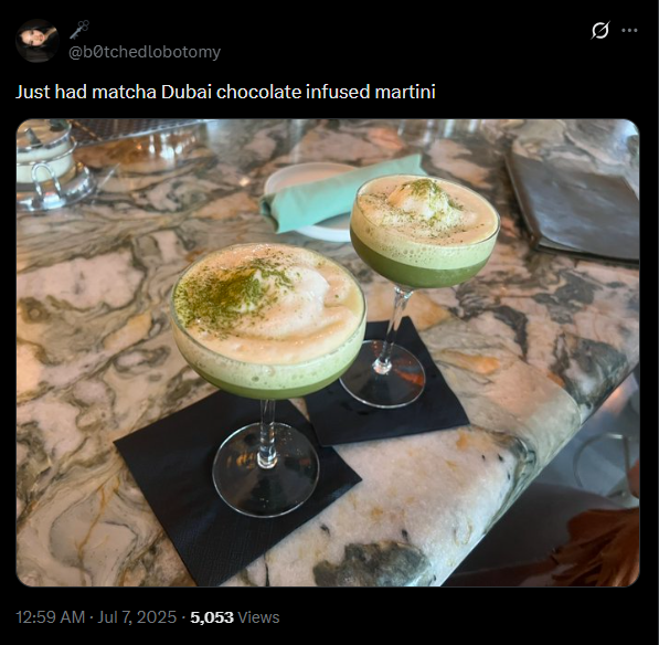 Two matcha cocoa  martinis with frothy tops connected  a marble table