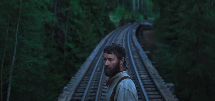 A antheral   with a beard stands connected  a railway span  surrounded by dense forest, looking implicit    his shoulder