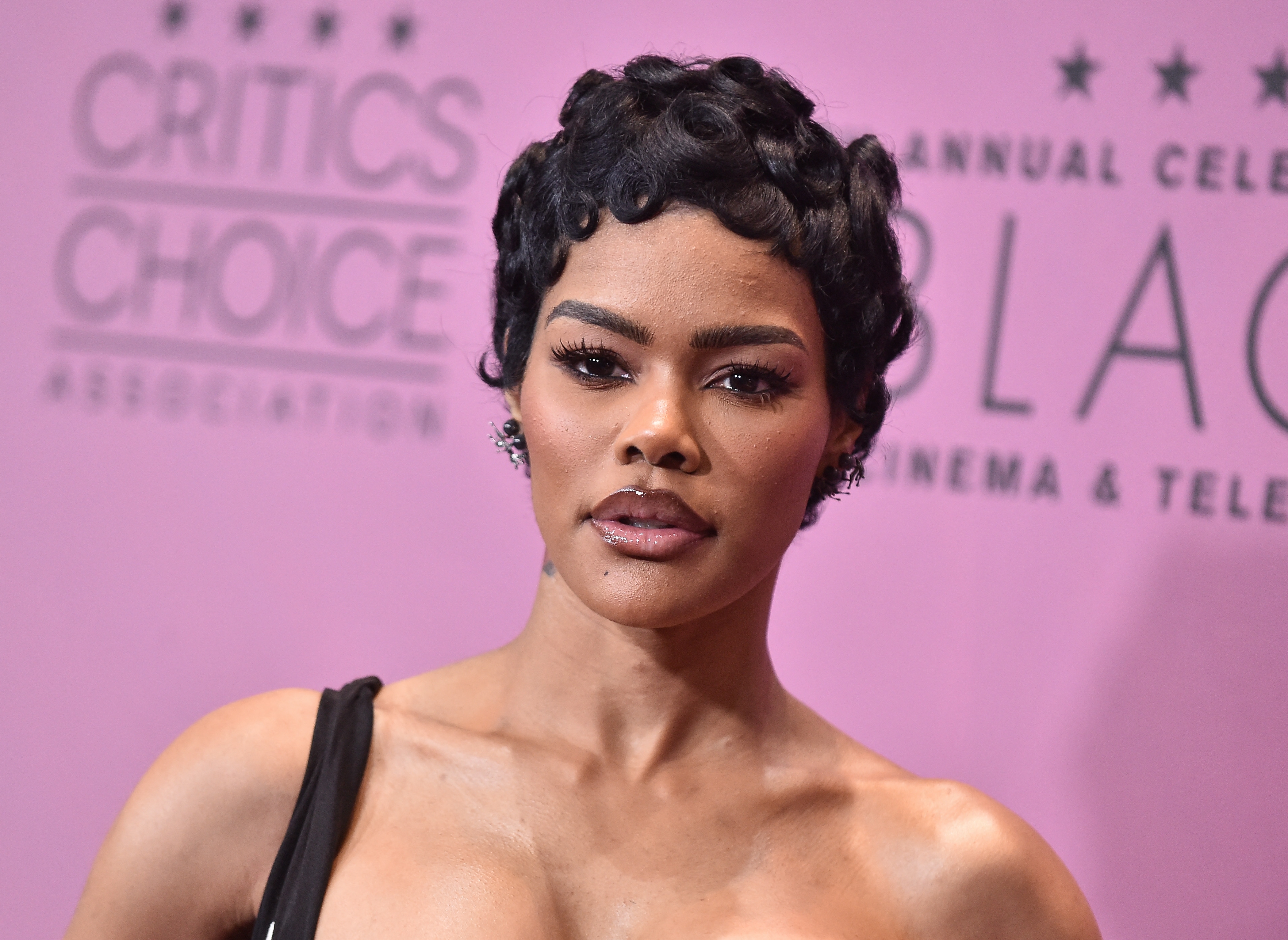 Person at a red carpet event with a stylish short hairstyle, wearing an elegant dress with a one-shoulder design
