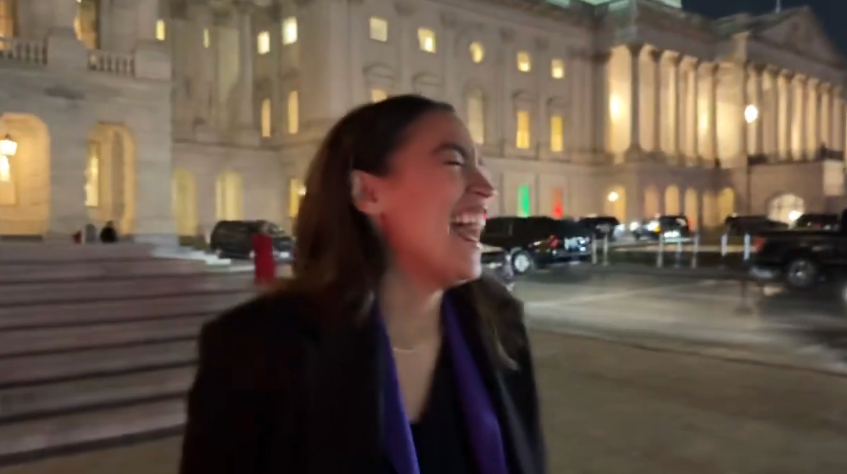 En person ler utenfor en storslått, opplyst bygning om natten, i et åpenhjertig øyeblikk som antyder glede eller overraskelse