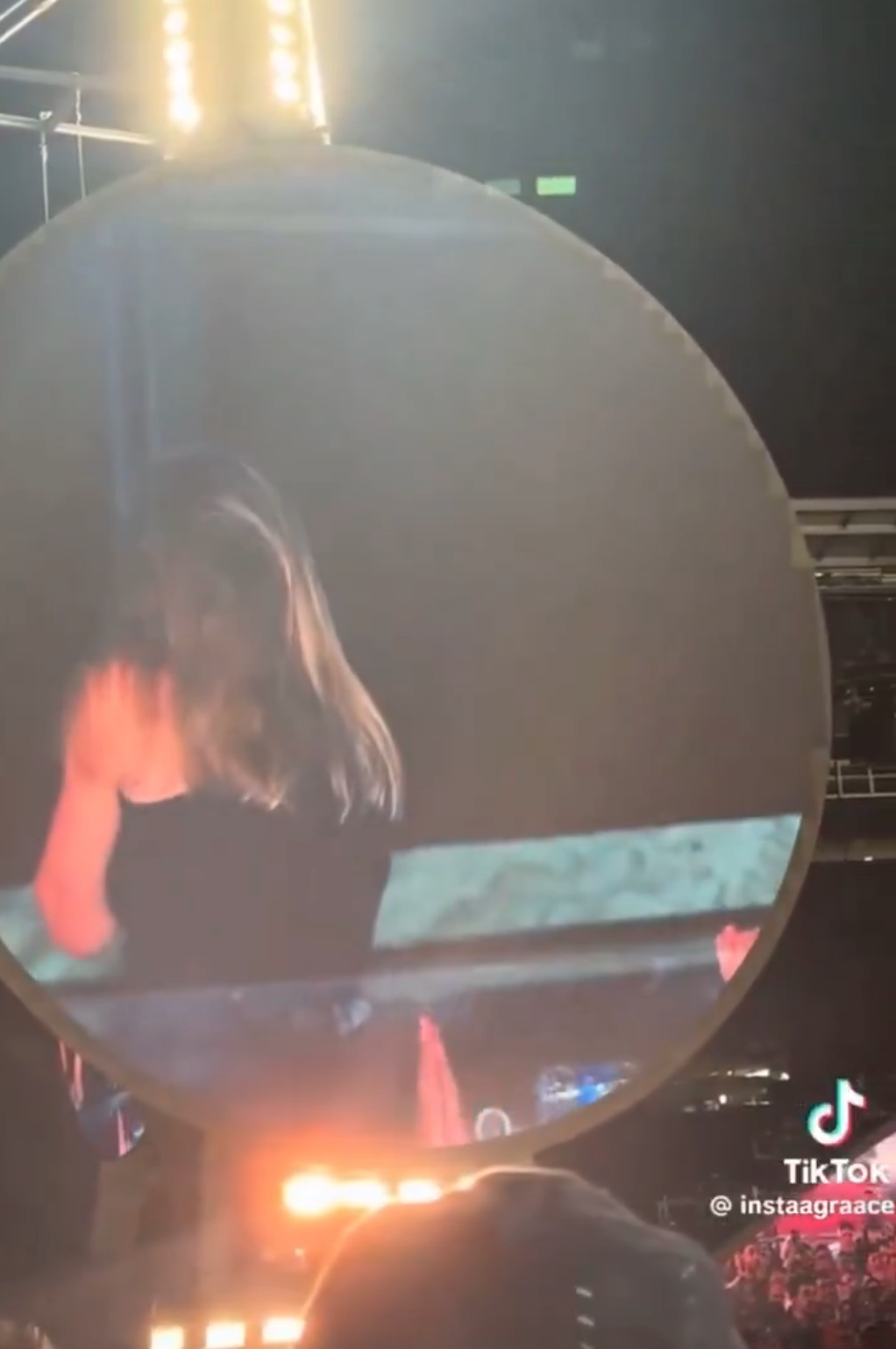 Person shown on a large screen at a concert, captured mid-performance with a focus on dynamic lighting and movement