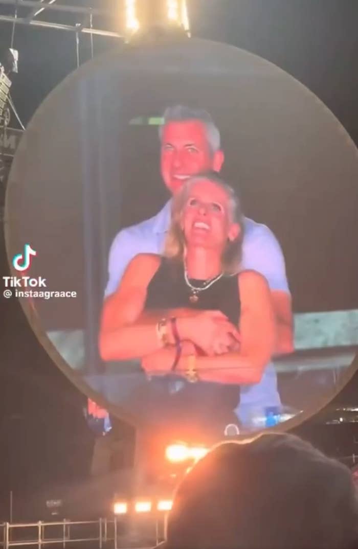 A couple joyfully embraces under stage lights at a concert, with a TikTok user tag visible on the side