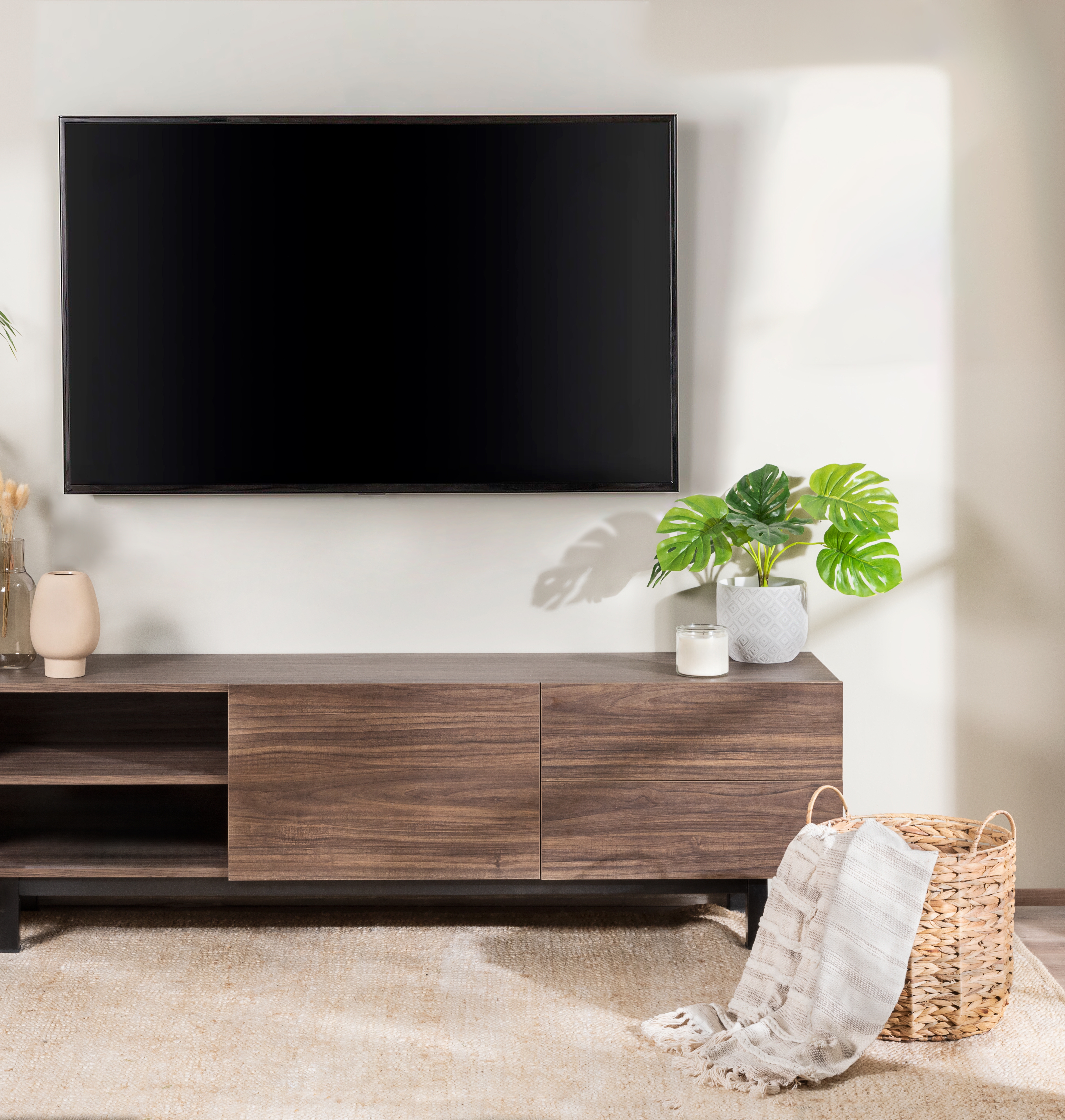 Modern living room with a mounted TV above a wooden media console, plants, and a woven basket with a blanket on the floor