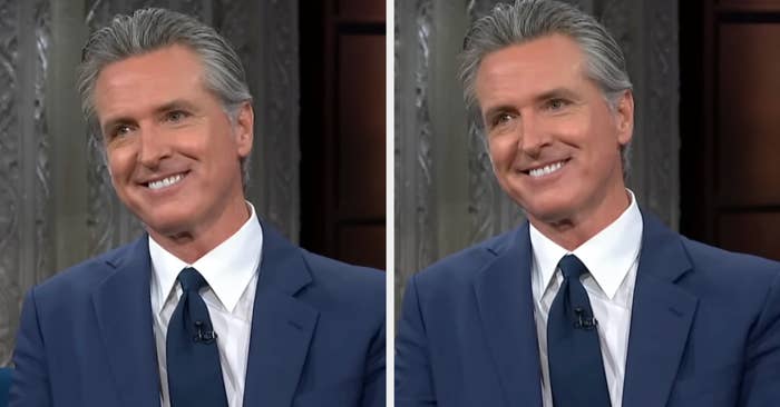 A person in a suit smiling during a talk show appearance, seated in a studio setting