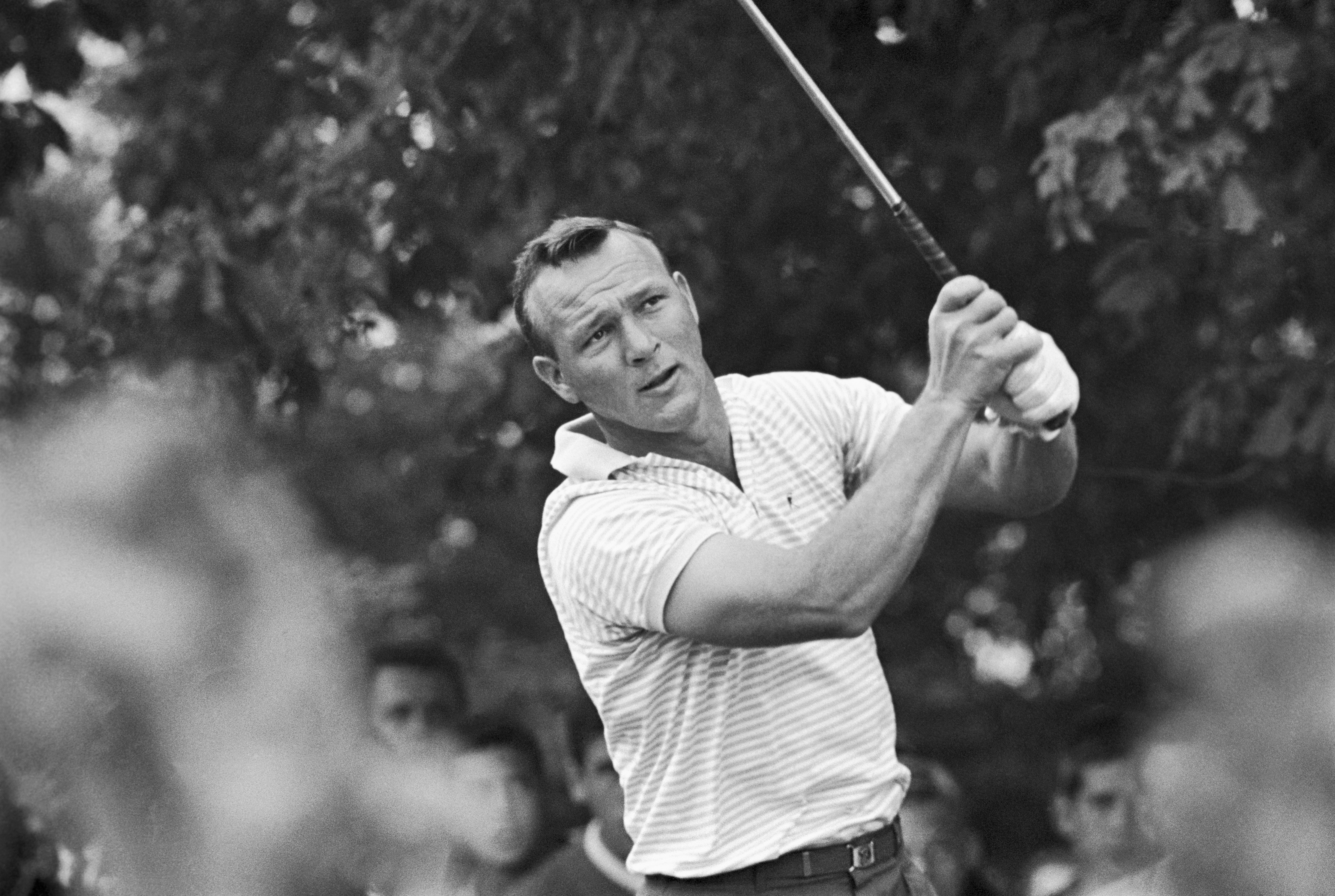Golfer swinging a nine  connected  a play  course, wearing a striped shirt; spectators are blurred successful  the background