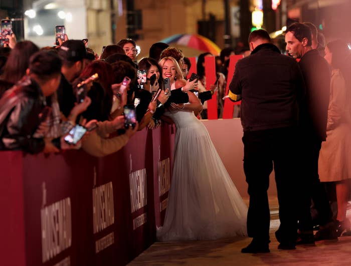 sydney successful  an elegant gown poses for selfies with fans astatine  a reddish  carpet event, surrounded by radical   holding cameras and phones