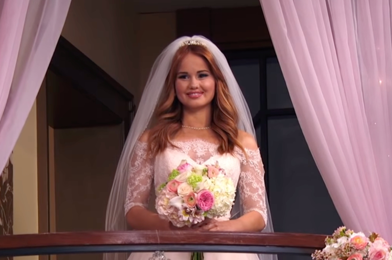 Person in a lace wedding dress holds a bouquet on a balcony with sheer curtains