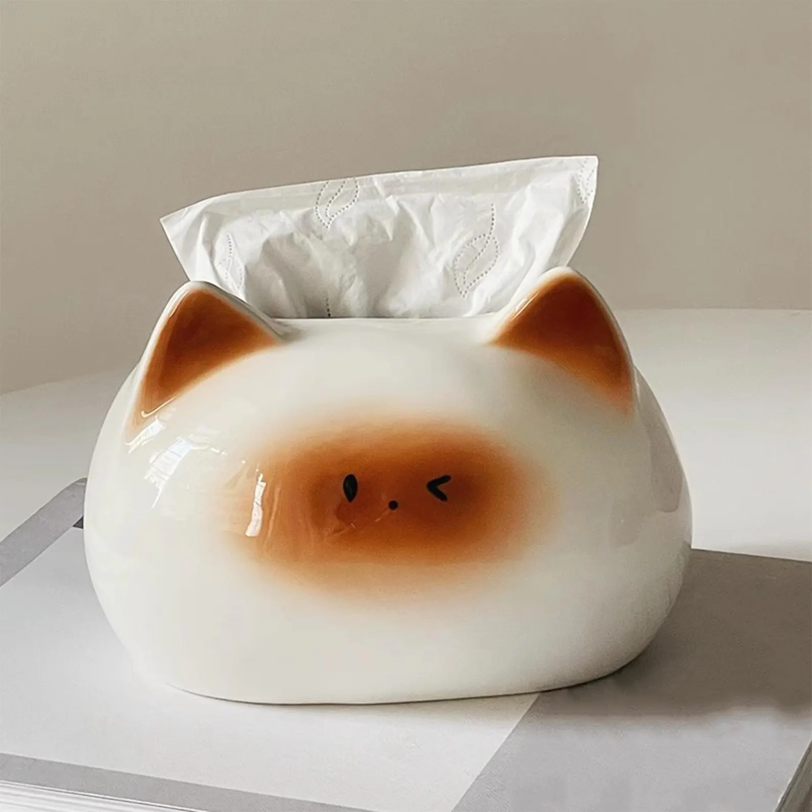 Cat-shaped tissue box with tissues inserted, featuring an adorable winking cat design, sits on a table