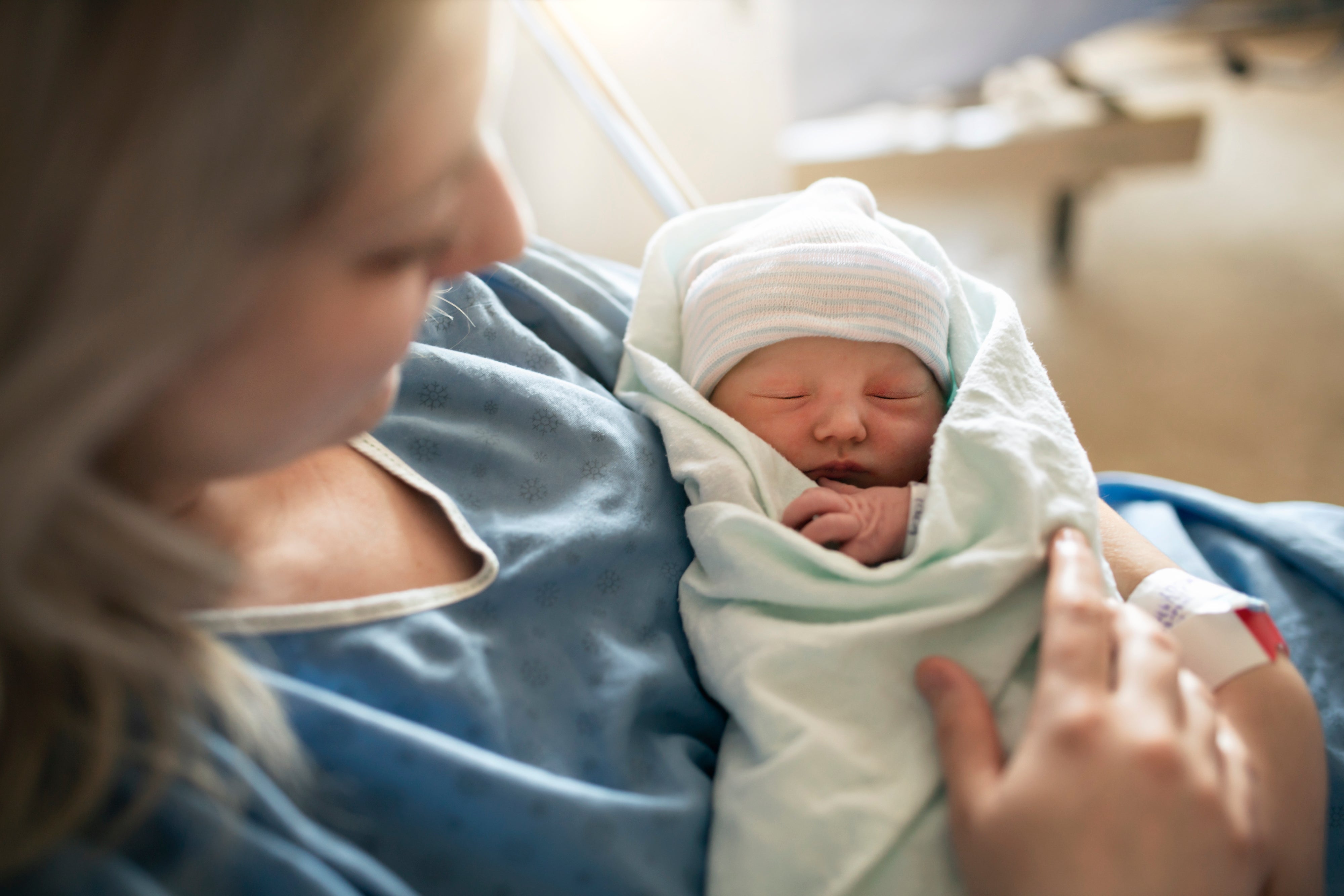 New mother cradles her newborn baby, wrapped in a blanket, in a hospital setting