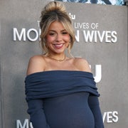 Jen Affleck in an off-shoulder dress cradles her baby bump at a media event
