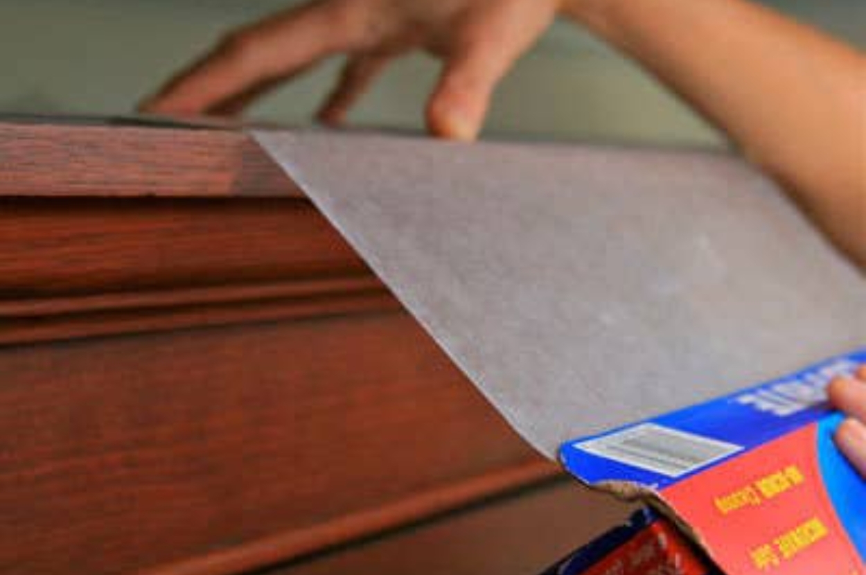 Person pulling wax paper from a box, holding it near a wooden surface, possibly preparing for a kitchen task