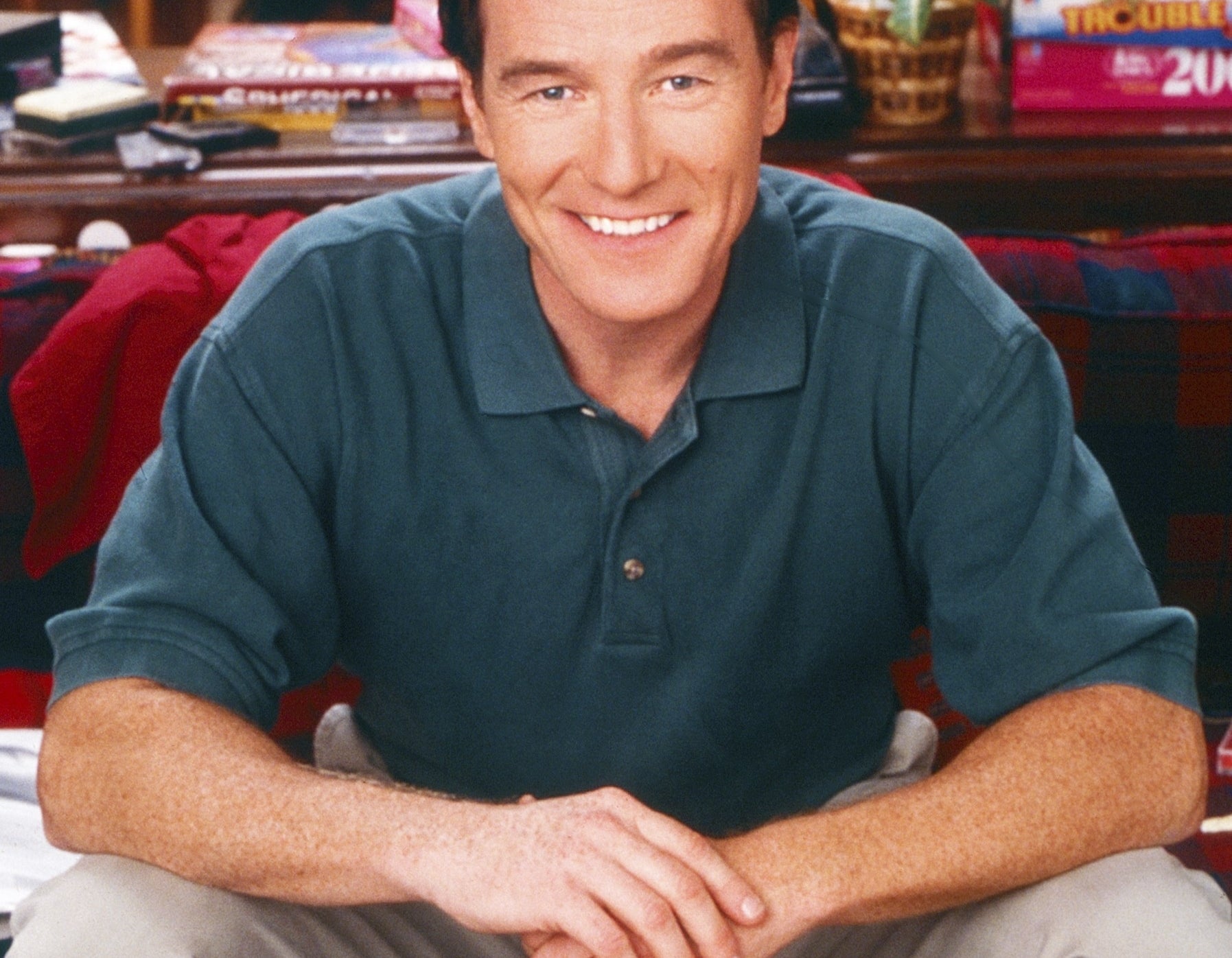Person sitting casually at home, wearing a polo shirt and khakis, surrounded by magazines