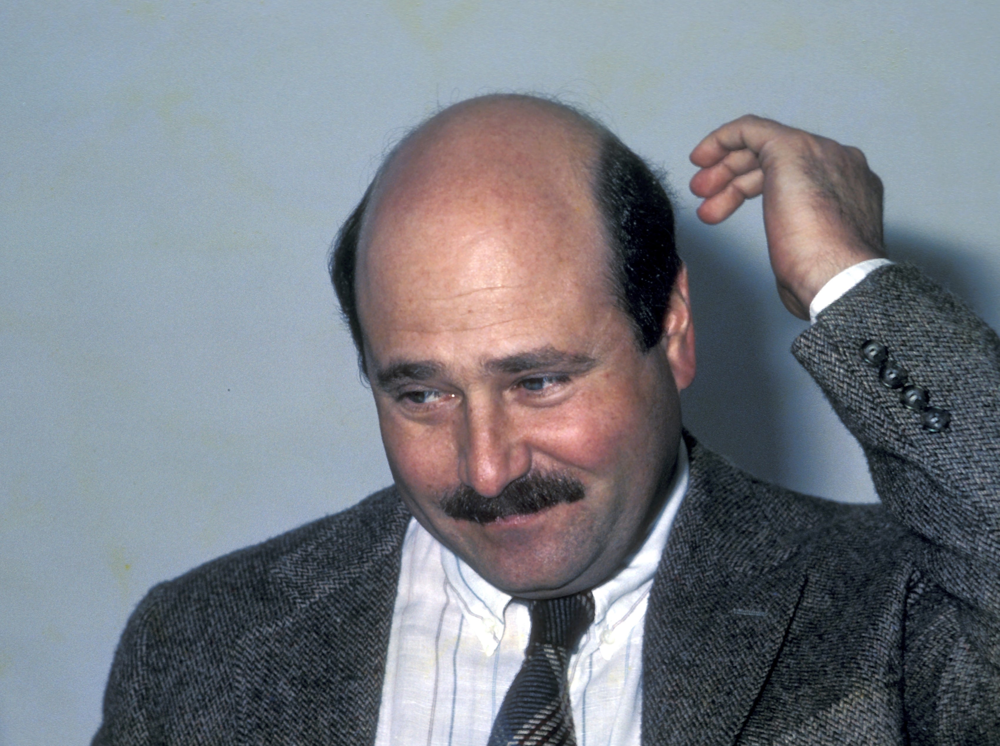 Bald antheral   successful  a suit   and necktie  with a mustache, scratching his caput  with a thoughtful expression