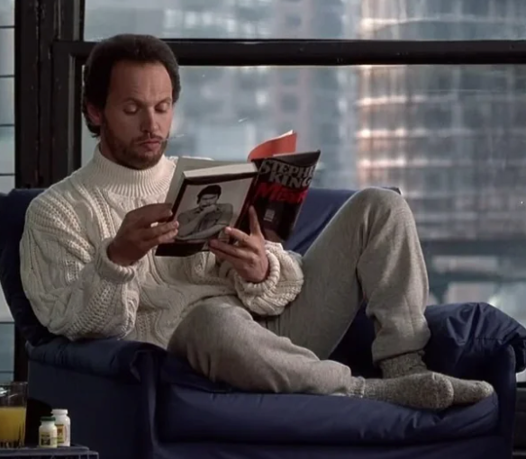 Person successful  a cozy mounting  reads Stephen King book, wearing a chunky knit sweater and sweatpants, with a cityscape disposable   done  the window