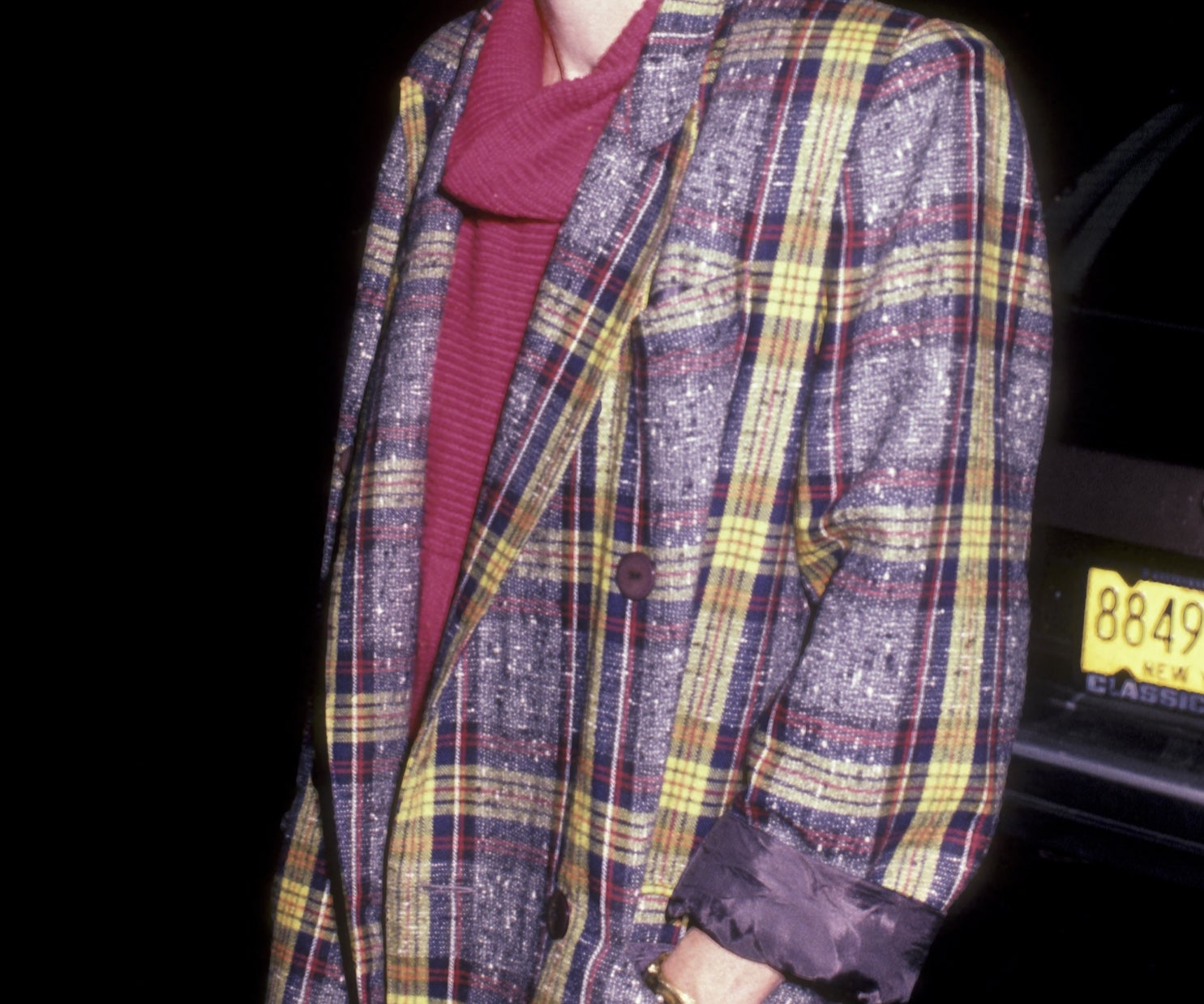 A idiosyncratic   wearing a plaid overgarment   implicit    a turtleneck and skirt, smiling, lasting  outdoors astatine  night