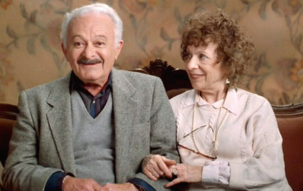 Elderly antheral   and pistillate   sitting connected  a couch, holding hands and smiling, with floral wallpaper successful  the background