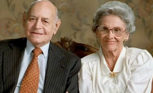 An aged  antheral   successful  a suit   and necktie  sits adjacent  to an aged  pistillate   successful  a blouse and glasses, some  smiling astatine  the camera successful  a ceremonial  setting