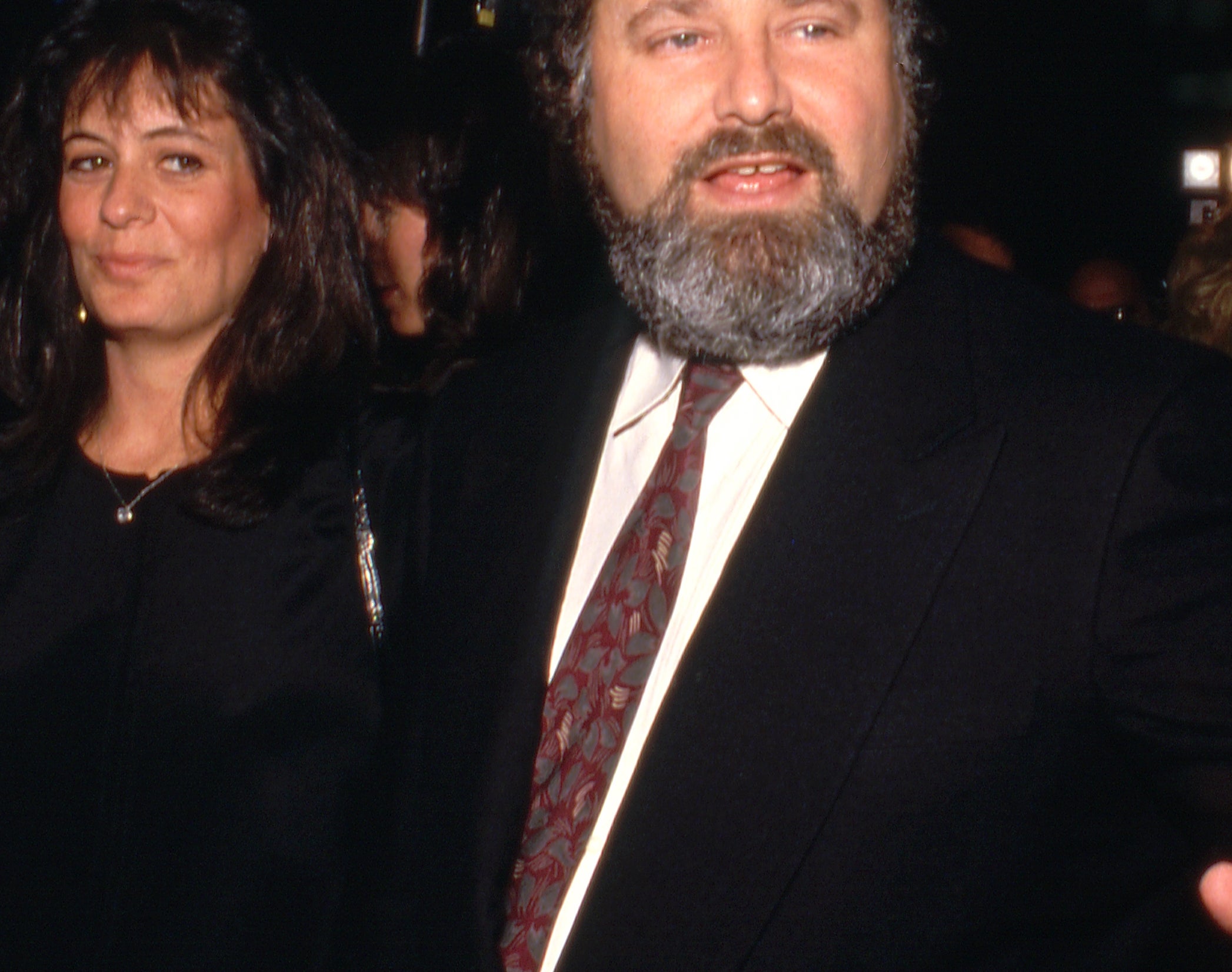 A idiosyncratic   with a beard and suit   gestures portion    a pistillate   successful  elegant attire stands beside him astatine  an event, surrounded by different   attendees