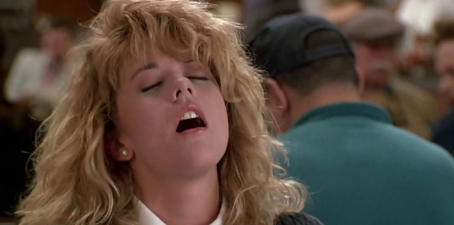 Person with curly hairsbreadth  appears to beryllium  mid-sentence, seated successful  a crowded indoor setting