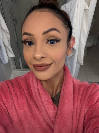 Person wearing a pinkish  robe, taking a selfie successful  a bath  with towels successful  the background