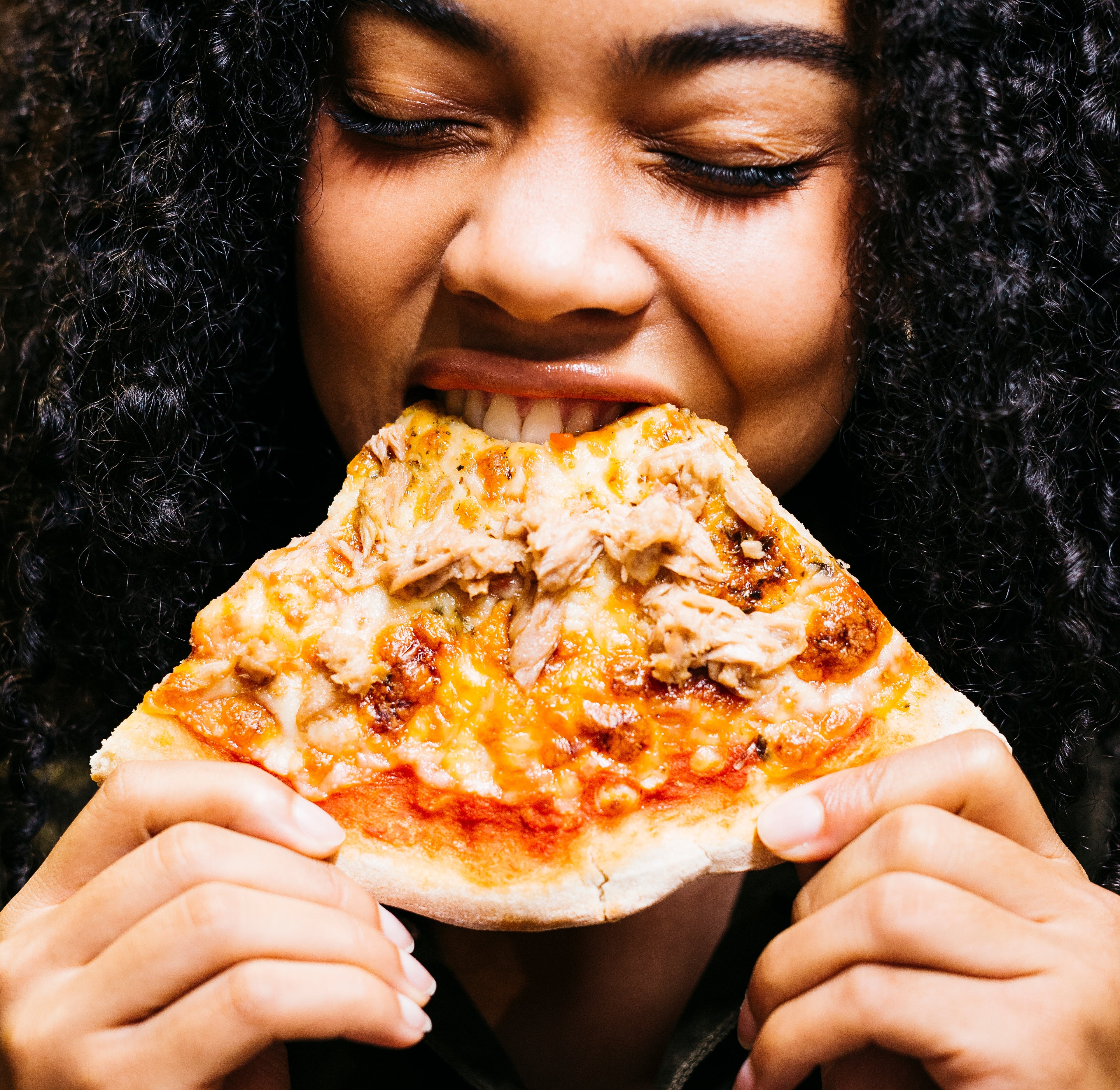 Person enjoying a slice of pizza, eyes closed, with a relaxed expression