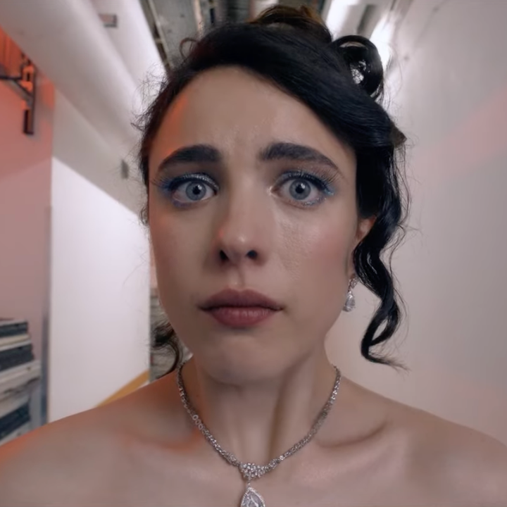 A woman with an anxious expression stands in a narrow hallway. She wears an elegant strapless dress and a necklace, suggesting a formal event