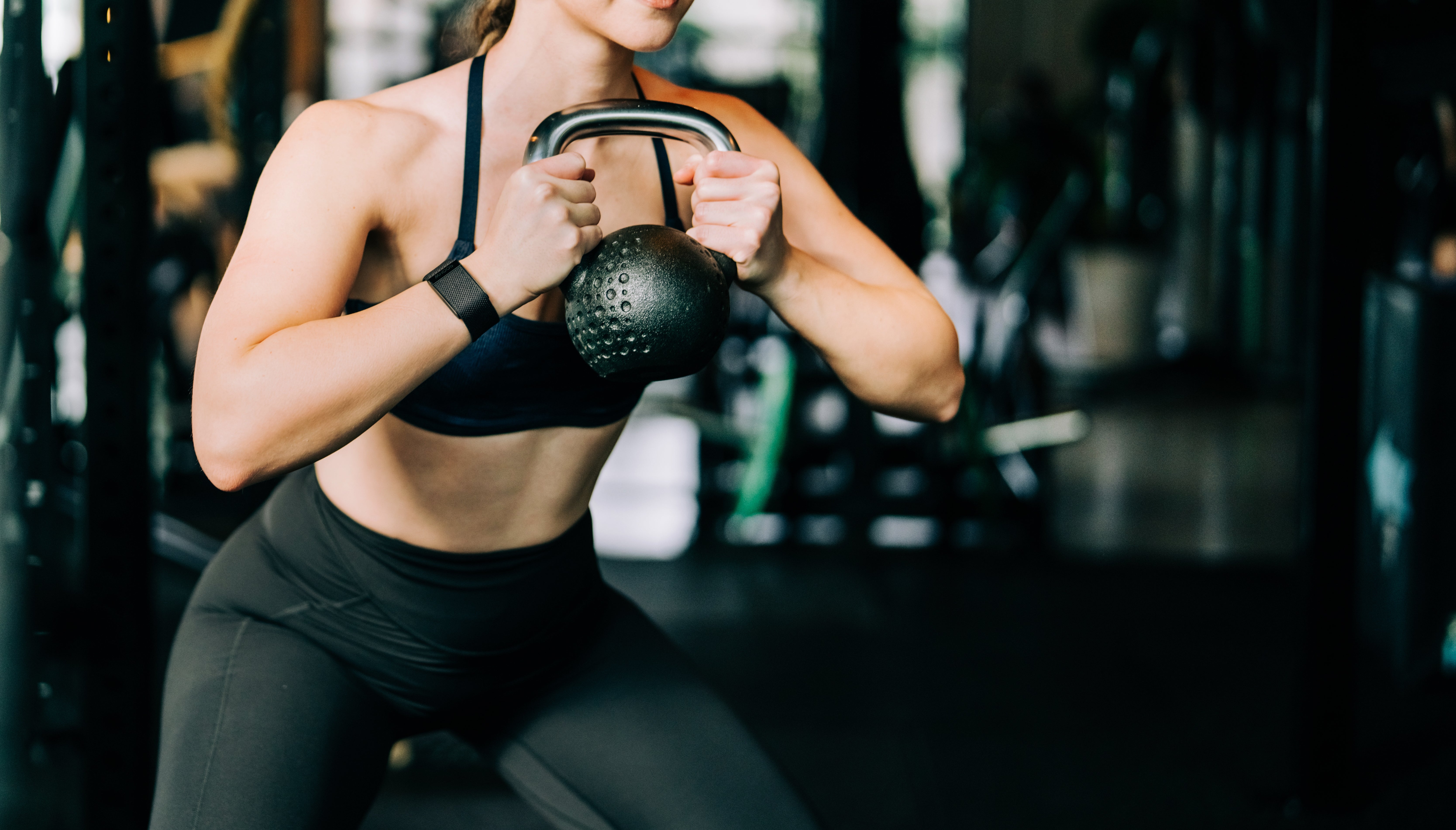Person exercising with kettlebell while wearing headphones and workout attire in a gym setting