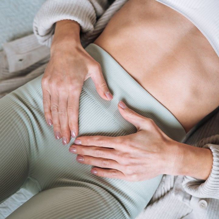Person lying down, hands on stomach over ribbed leggings, wearing a cozy cardigan and a top