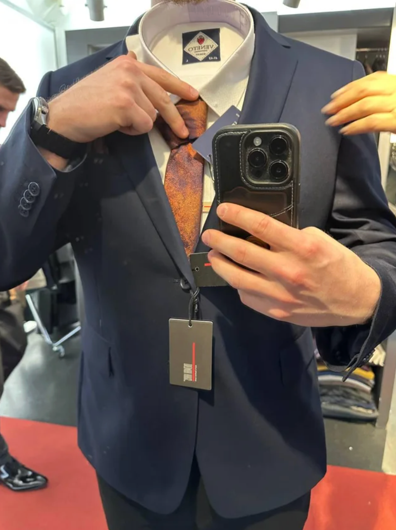 Person successful  a suit   stands successful  beforehand   of a mirror, adjusting an orangish  necktie  with a tag, portion    different  idiosyncratic   assists