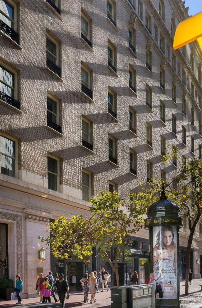 Street country   with radical   walking by a ample  gathering  with chiseled  shadiness   patterns created by its windows. An advertisement is connected  a adjacent    pillar