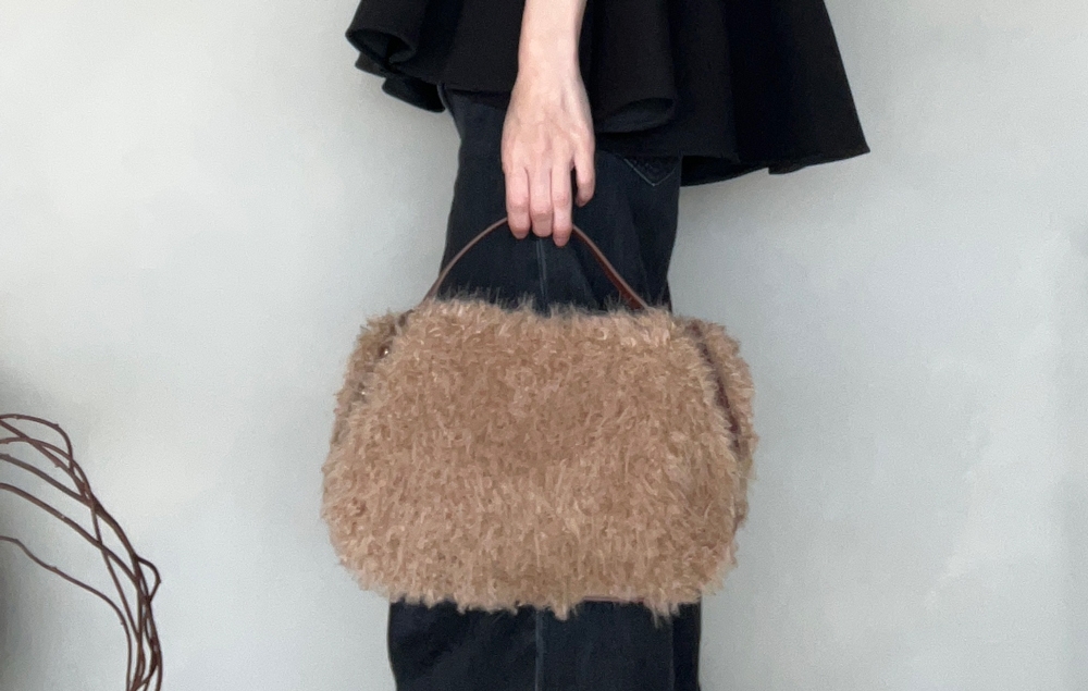 Person holding a fluffy handbag, wearing a knee-length skirt or dress