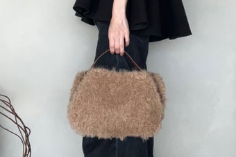 Person holding a fluffy handbag, wearing a knee-length skirt or dress