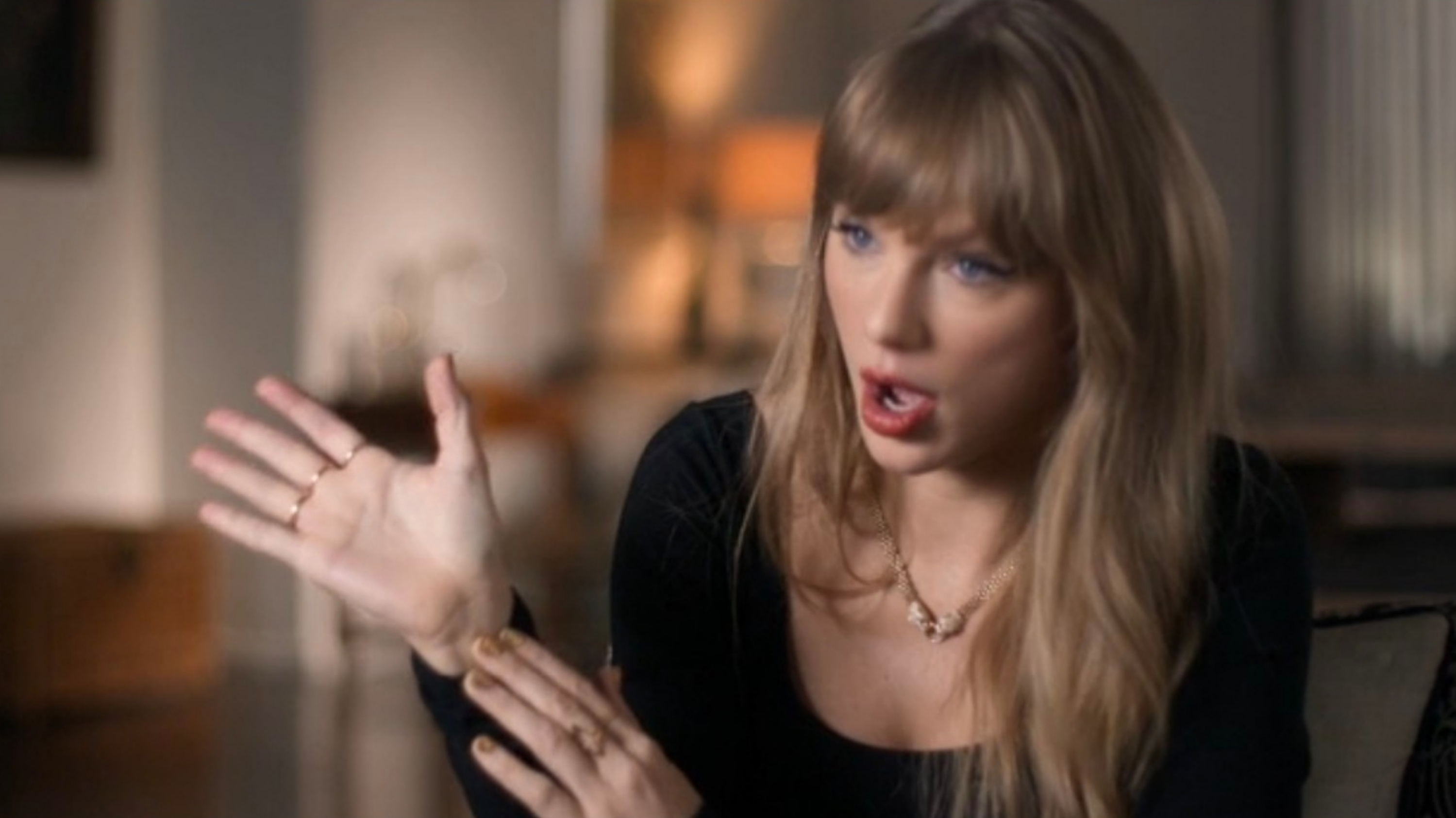 A idiosyncratic   with agelong  hairsbreadth  gestures expressively portion    speaking, seated successful  a country   with brushed  lighting. They deterioration  a achromatic  apical  and a necklace