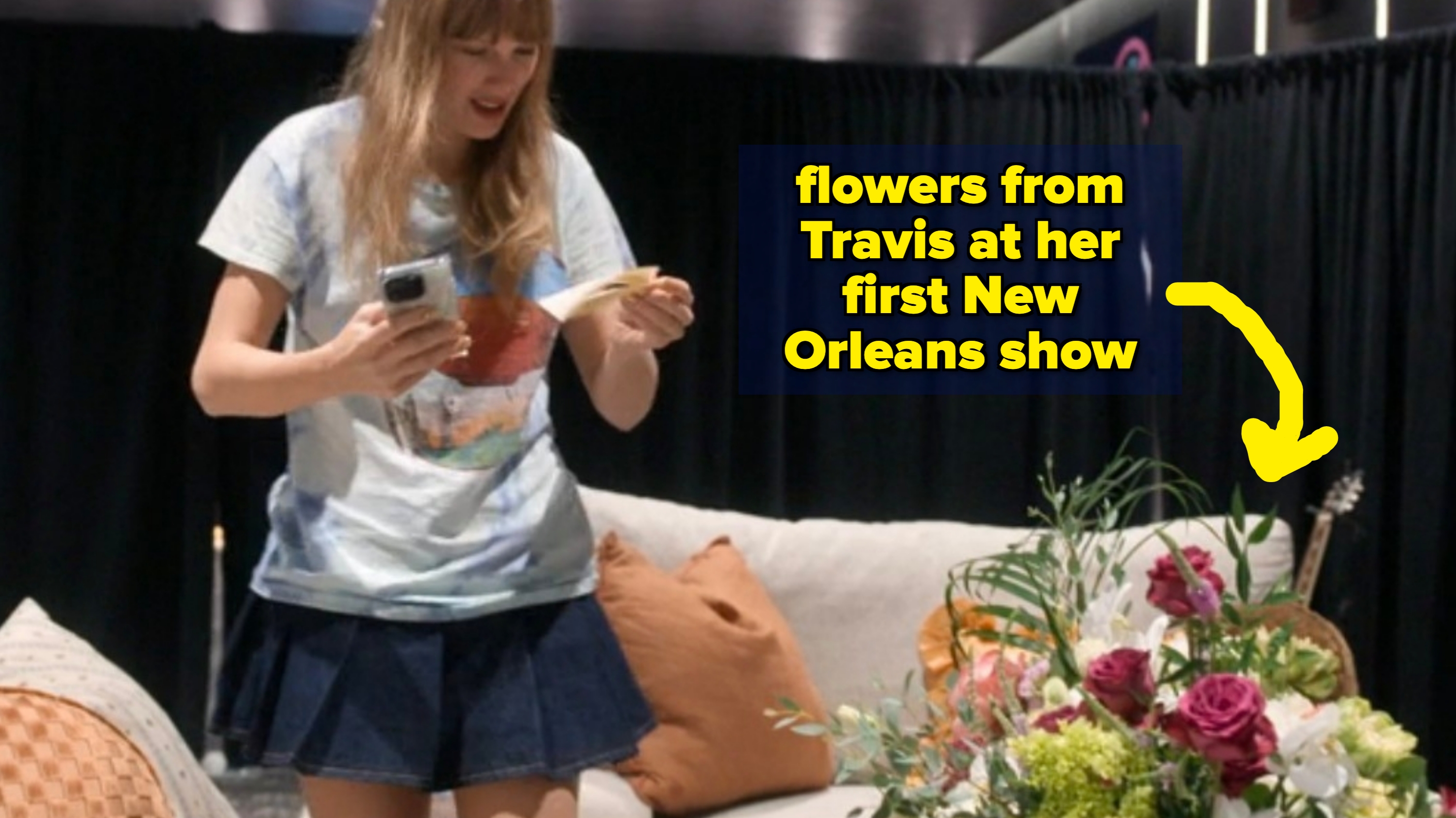 A idiosyncratic   successful  a casual T-shirt and skirt stands smiling successful  a cozy room, looking astatine  a missive  portion    holding a phone, with a bouquet of flowers nearby